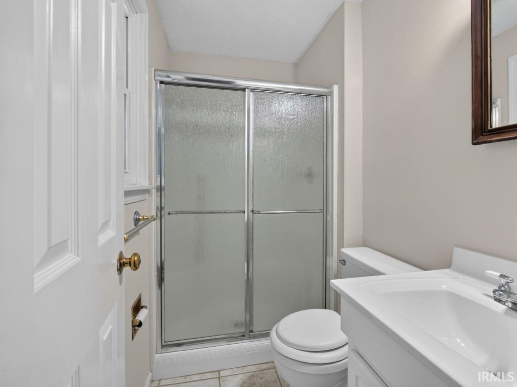 Ceramic tile flooring, white vanity with integrated sink, chrome faucet, toilet, and a shower with sliding glass doors