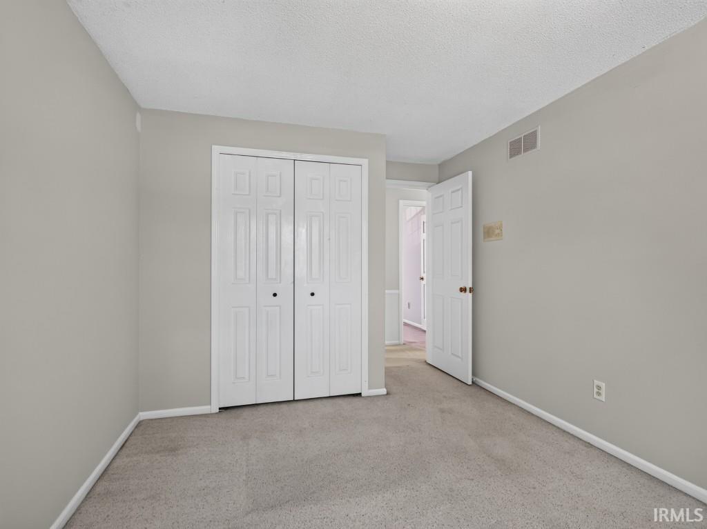 Neutral wall paint, textured ceiling, carpeted flooring, and paneled bifold closet doors