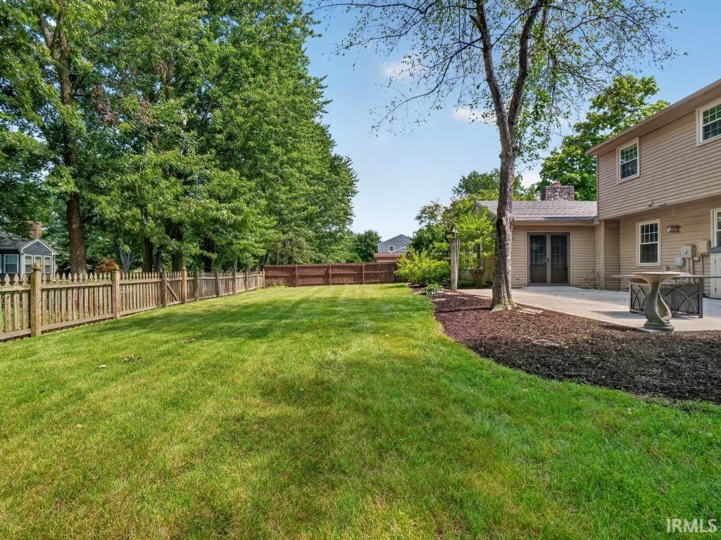Expansive lawn area with a picket fence, mature trees, a concrete patio, and a wood-paneled exterior