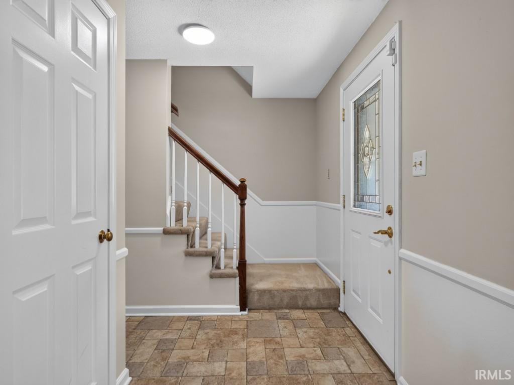 Foyer featuring patterned tile flooring, wainscoting, and a paneled front door with decorative glass