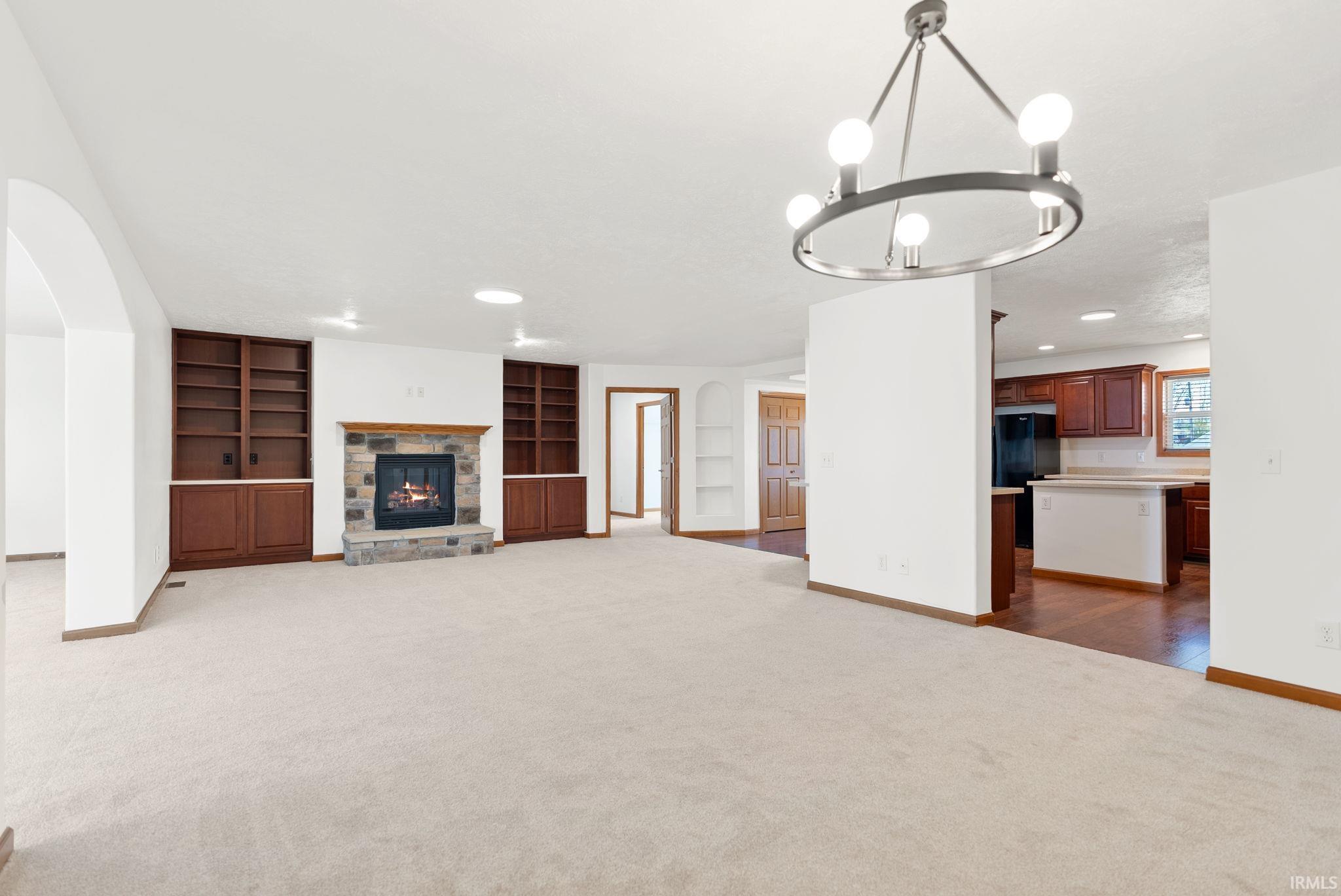 Spacious living area featuring a stone-clad fireplace with wood mantle, built-in wooden shelving, and a contemporary chandelier