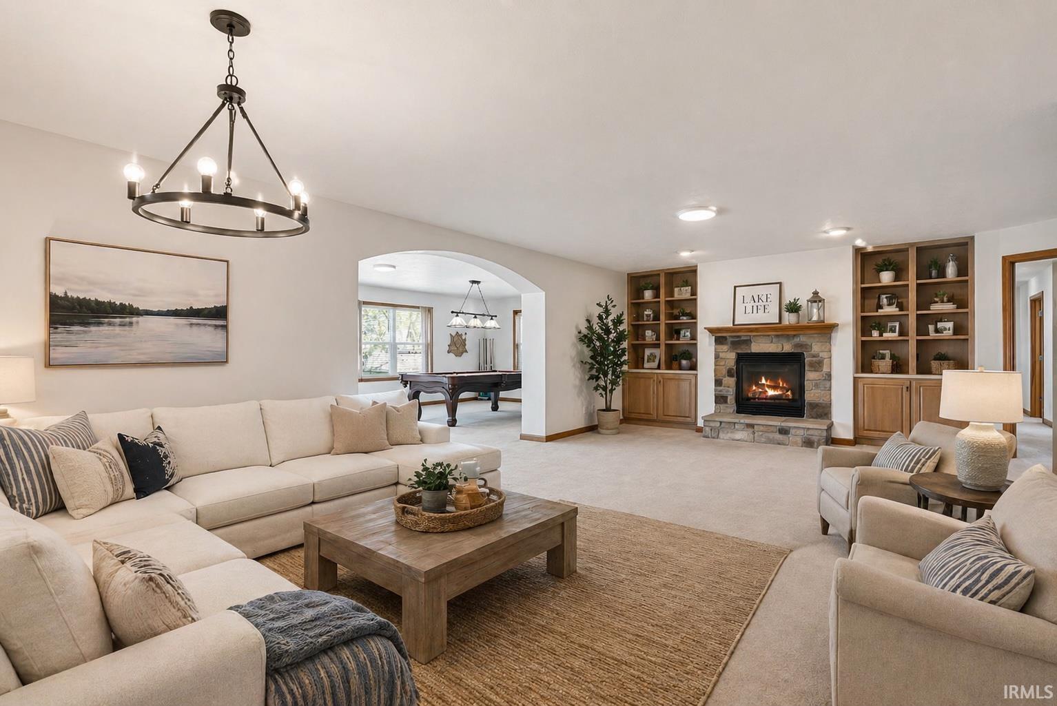 Spacious living area featuring a stone fireplace with a wood mantel, built-in shelving, an arched doorway, and a contemporary chandelier