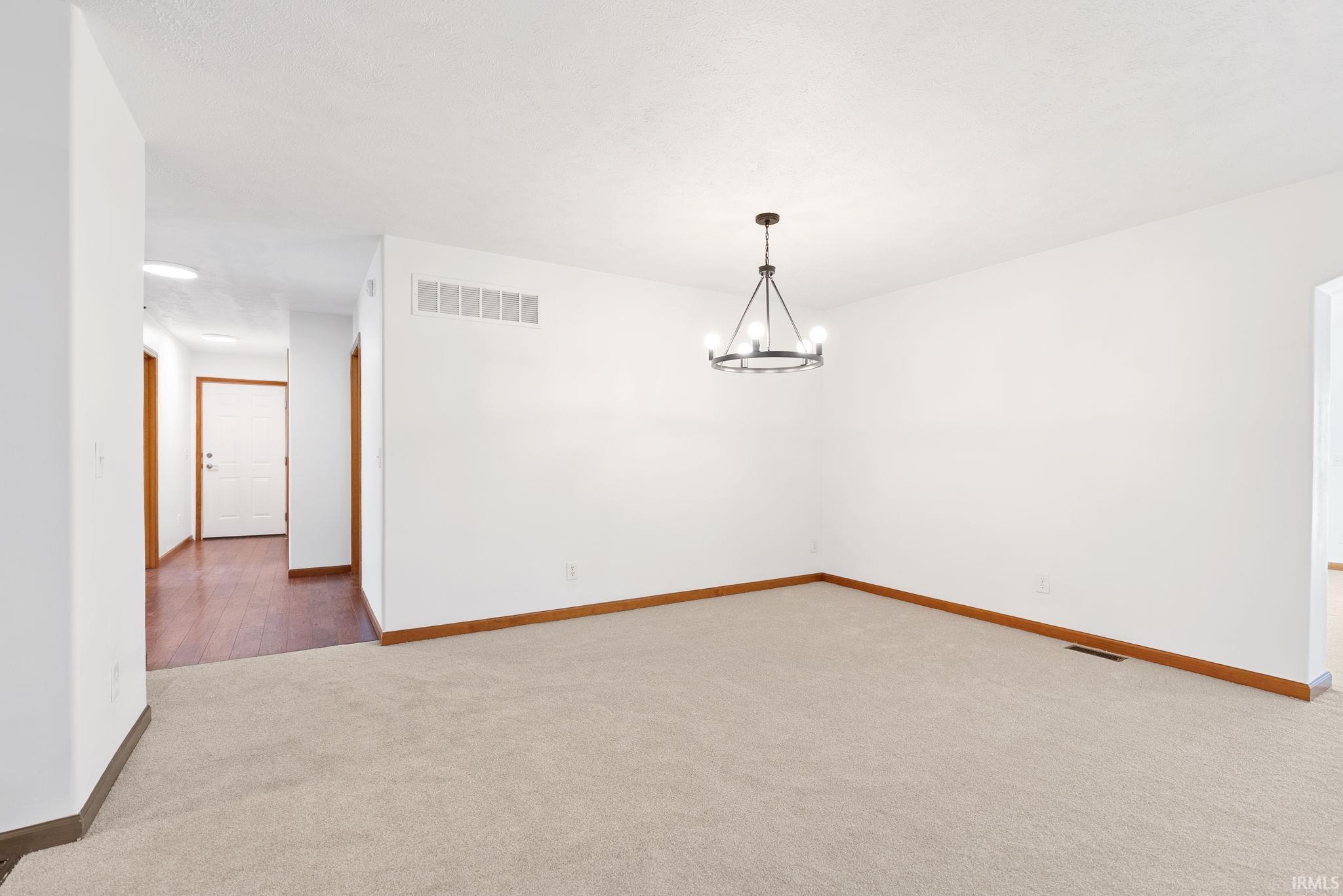 Spacious room featuring neutral carpeting and a contemporary chandelier