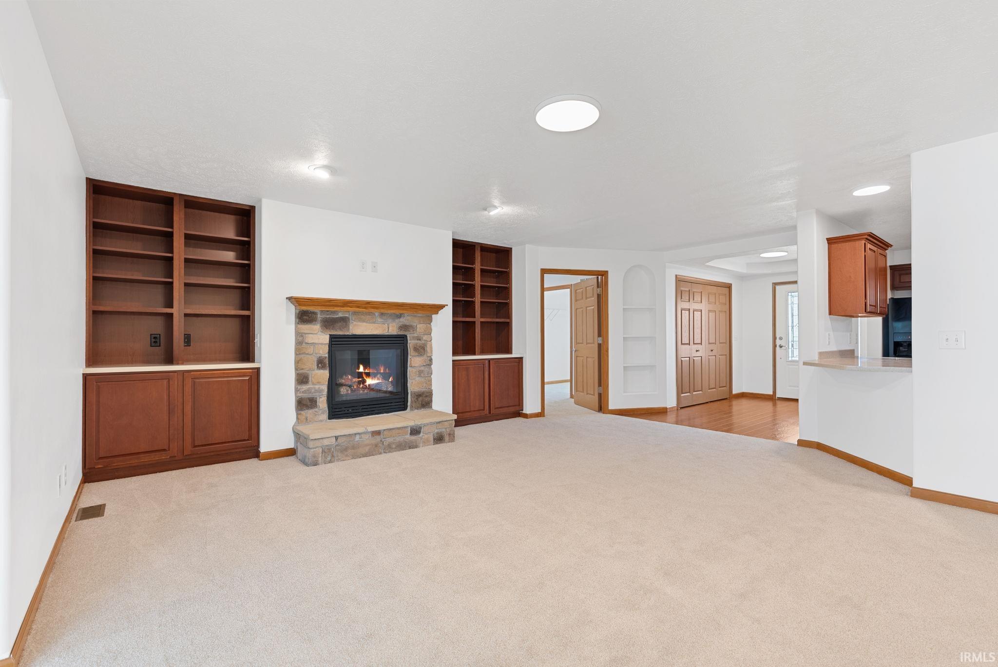 Living area with a stone-faced fireplace, integrated wood-finish cabinetry, built-in shelving, and recessed lighting