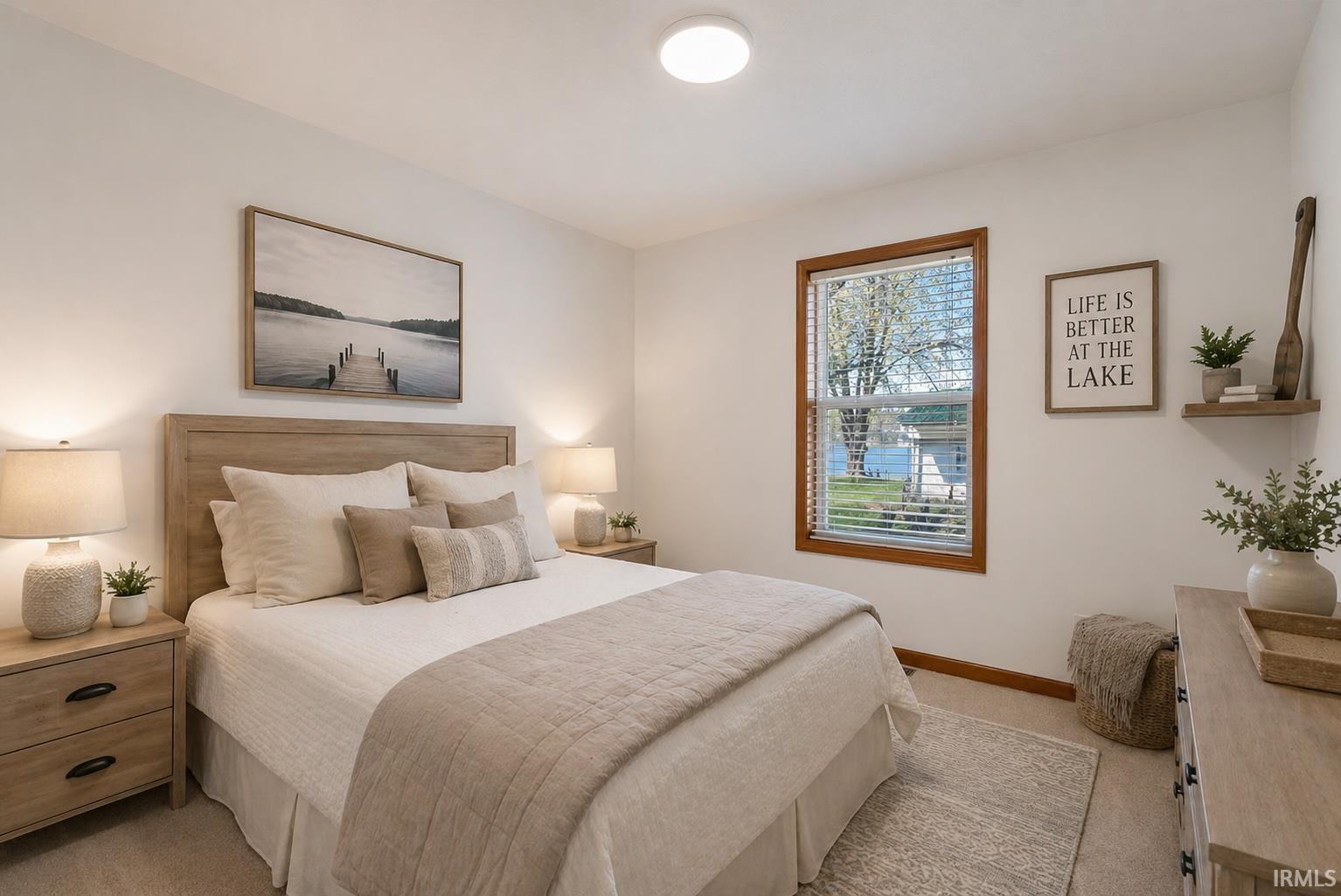 Bright bedroom featuring a single window with wood trim, ceiling-mounted light fixture, light-toned carpeting, and white painted walls