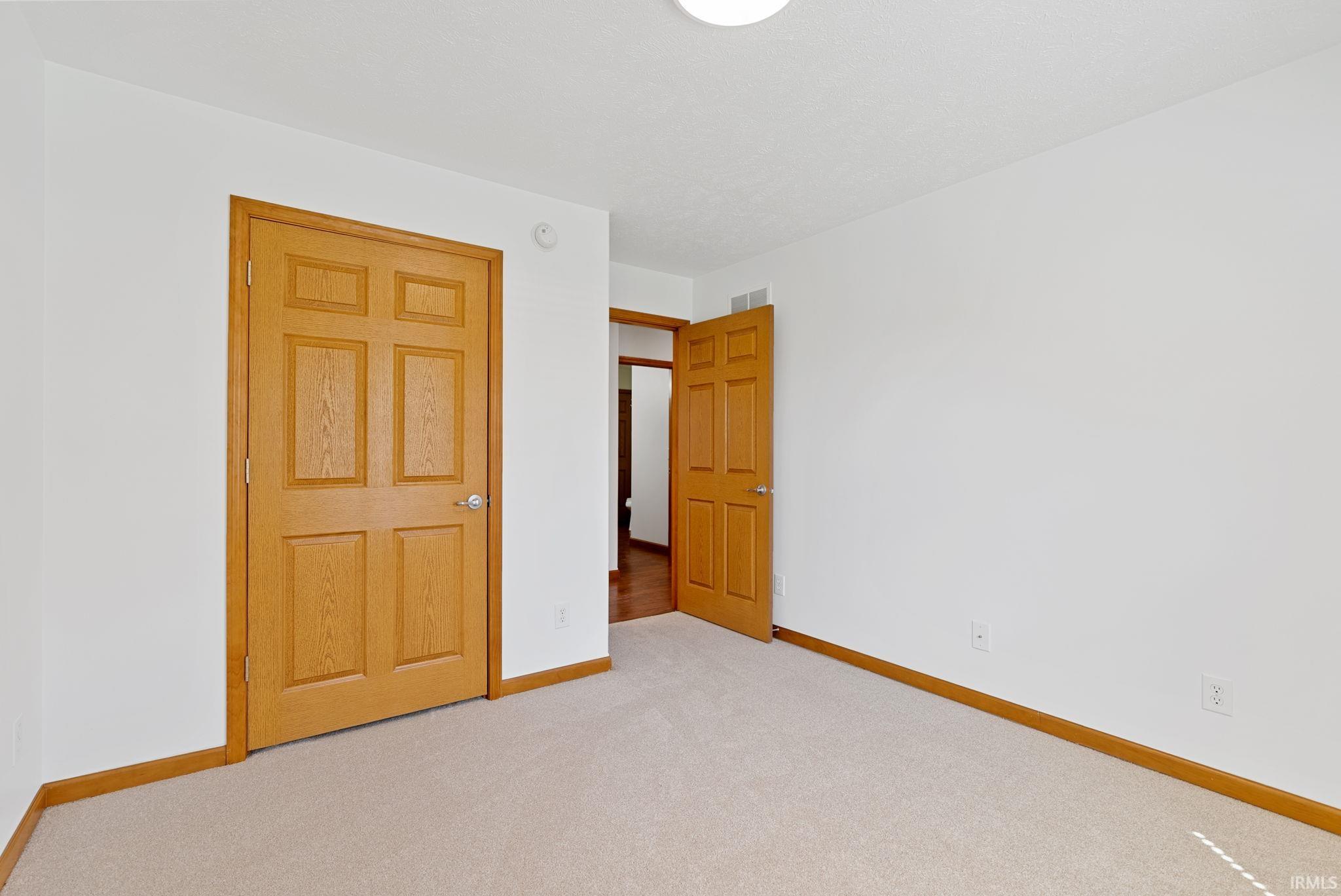 Carpeted interior room featuring light wood-finish doors and trim, white walls, and a flush mount ceiling light fixture