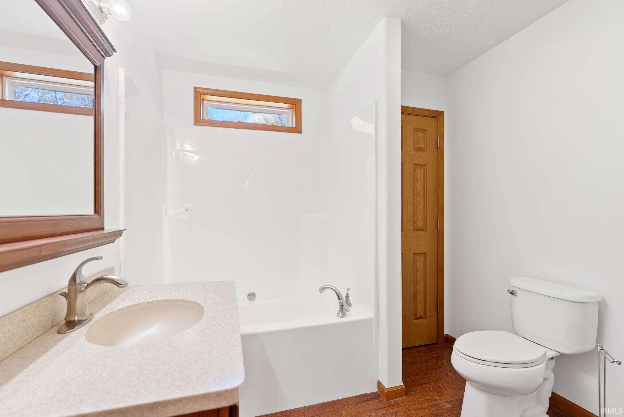 Bathroom featuring a white bathtub/shower combination, a vanity with an integrated sink and light-toned countertop, and wood-finish flooring