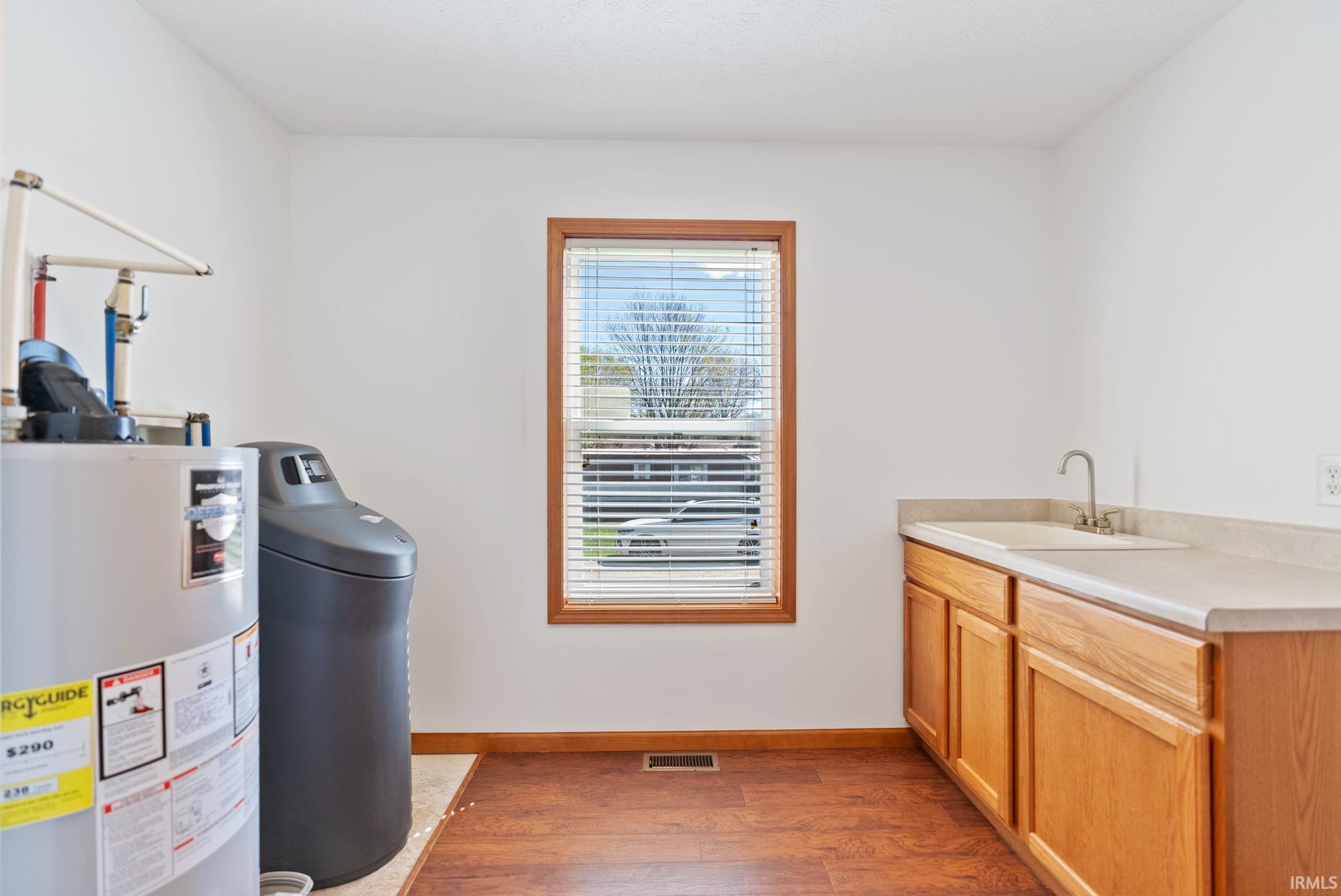 Utility room featuring wood-finish flooring, a single window with wood trim, white walls, built-in cabinetry, and a utility sink with a gooseneck faucet