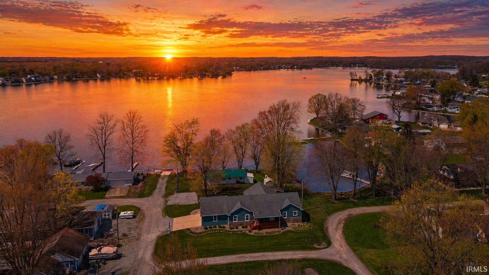 Waterfront property featuring a residential structure with an attached garage, a private boat dock, and a landscaped yard with mature trees