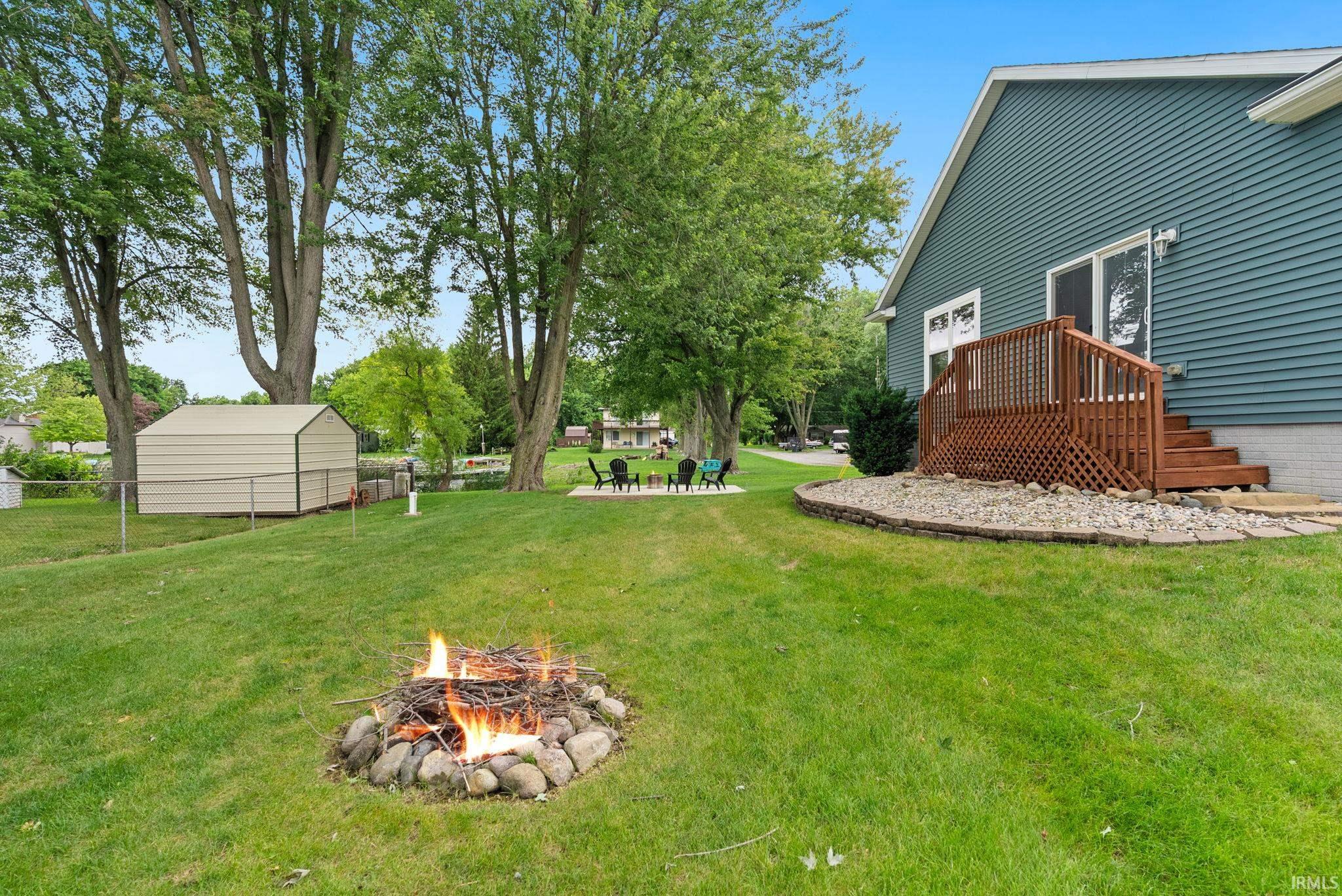 Expansive backyard featuring a stone fire pit, extensive green lawn, and mature trees