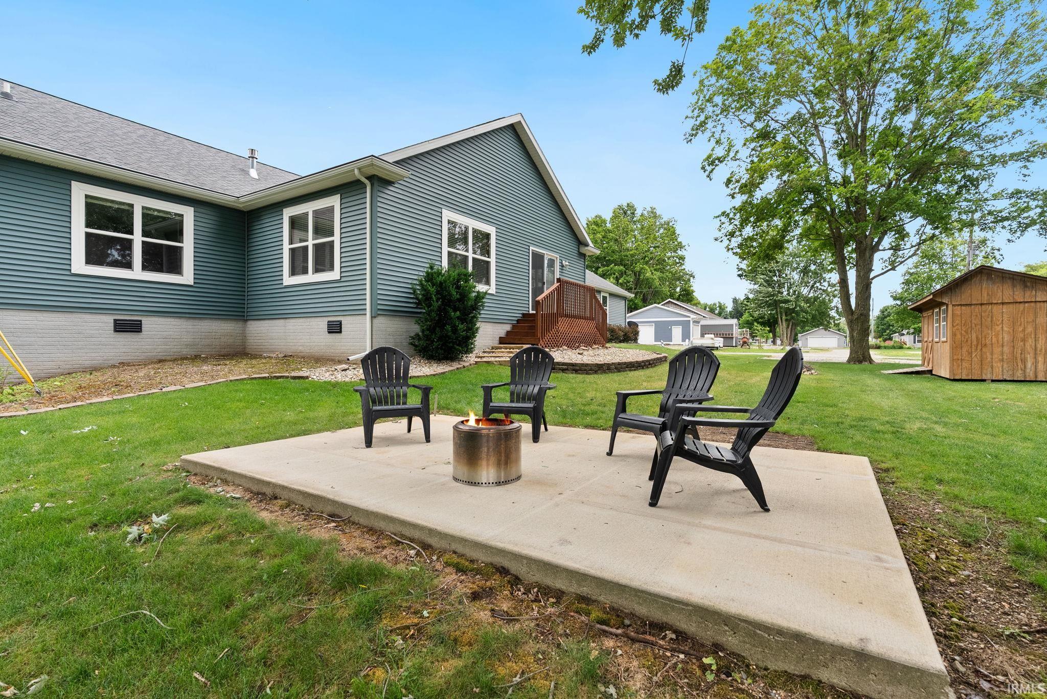 Outdoor concrete patio with fire pit, surrounded by a lush green lawn