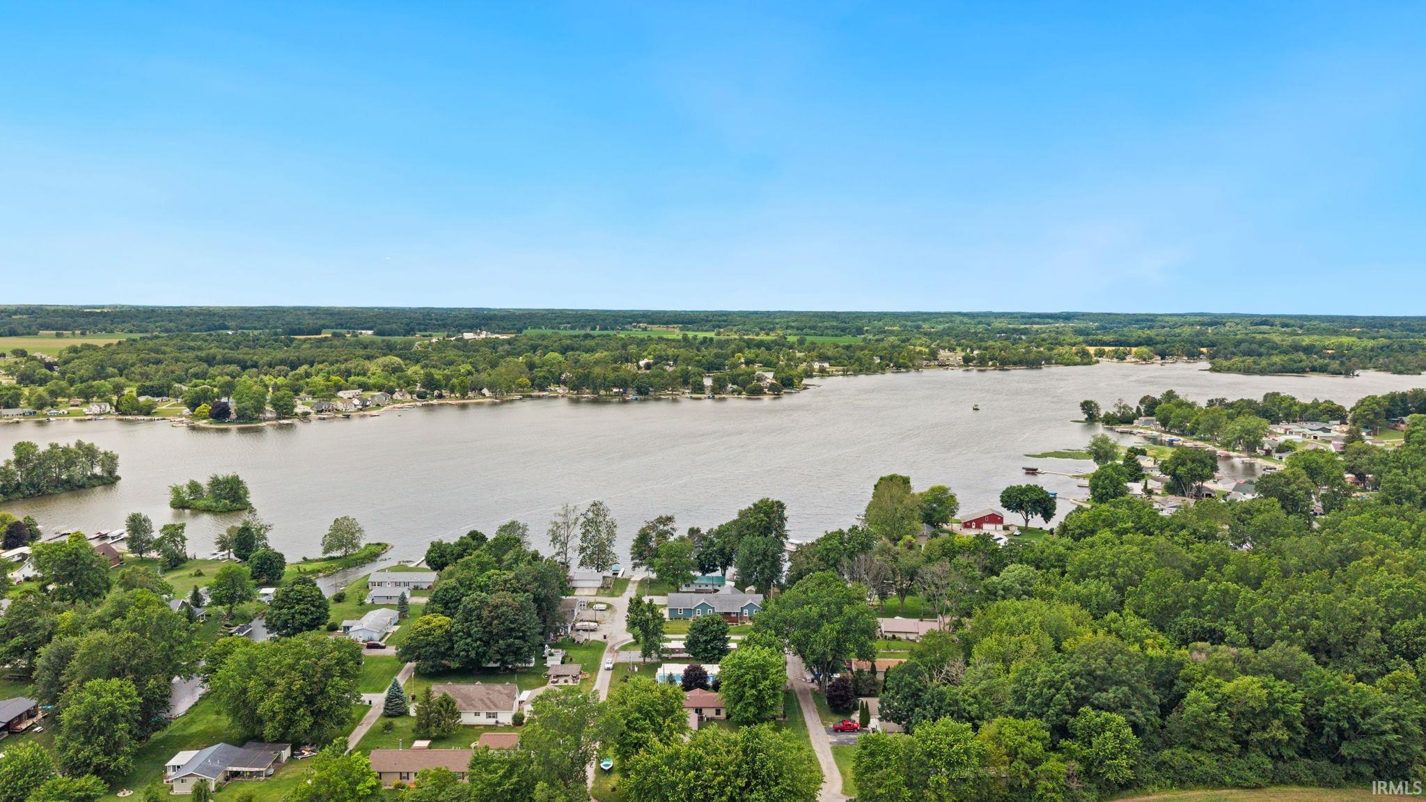 Expansive lakefront setting featuring a clear blue sky, mature green trees, and residential properties bordering the water
