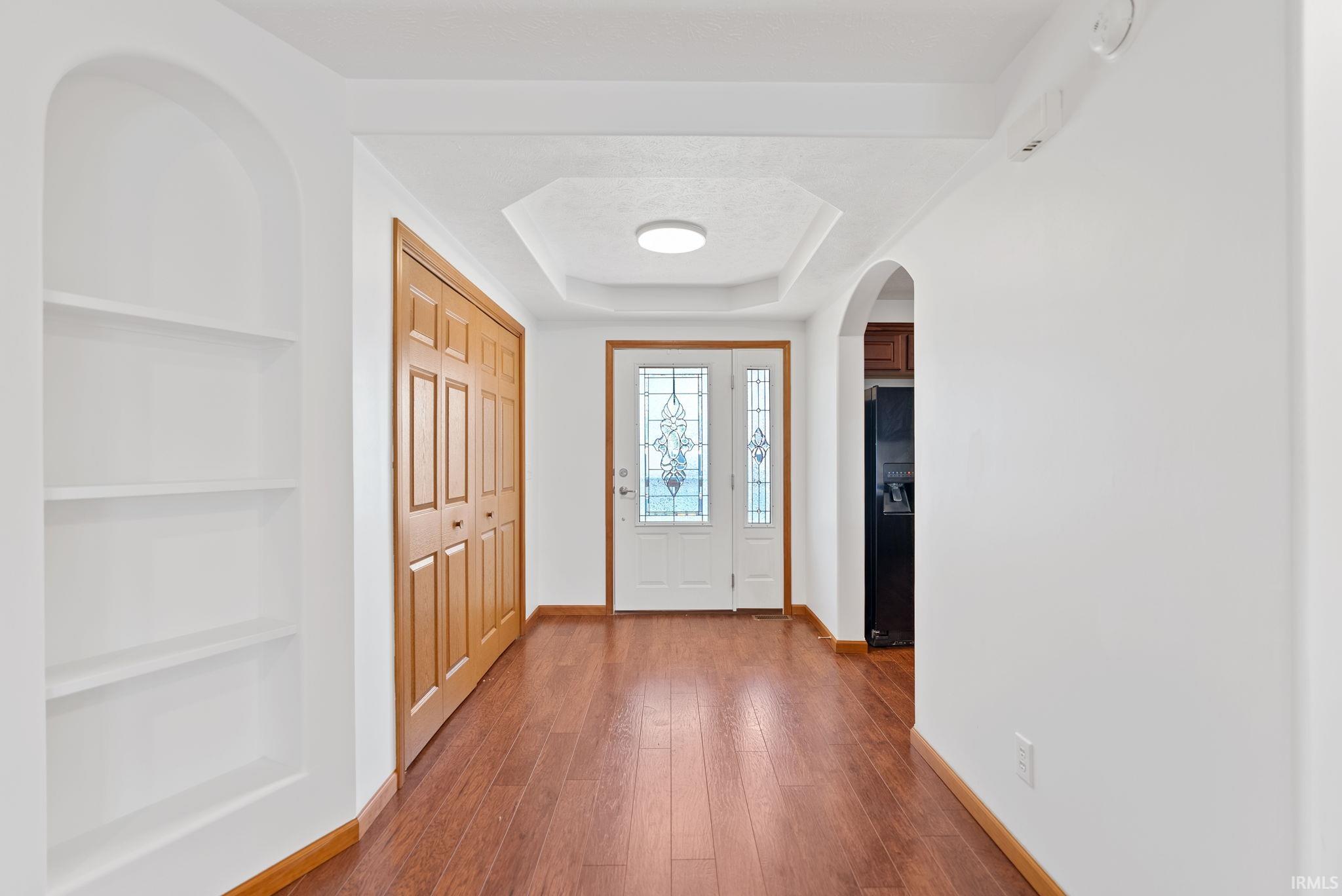 Entryway featuring wood-finish flooring, a decorative tray ceiling with flush-mount lighting, and a double-door entry with leaded glass inserts