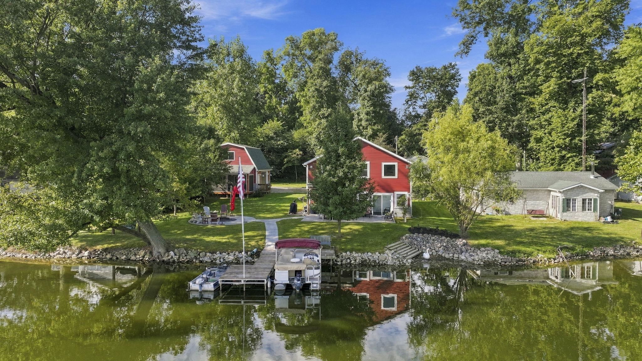 Waterfront property featuring a private dock, two distinct structures, mature trees, and a grassy yard