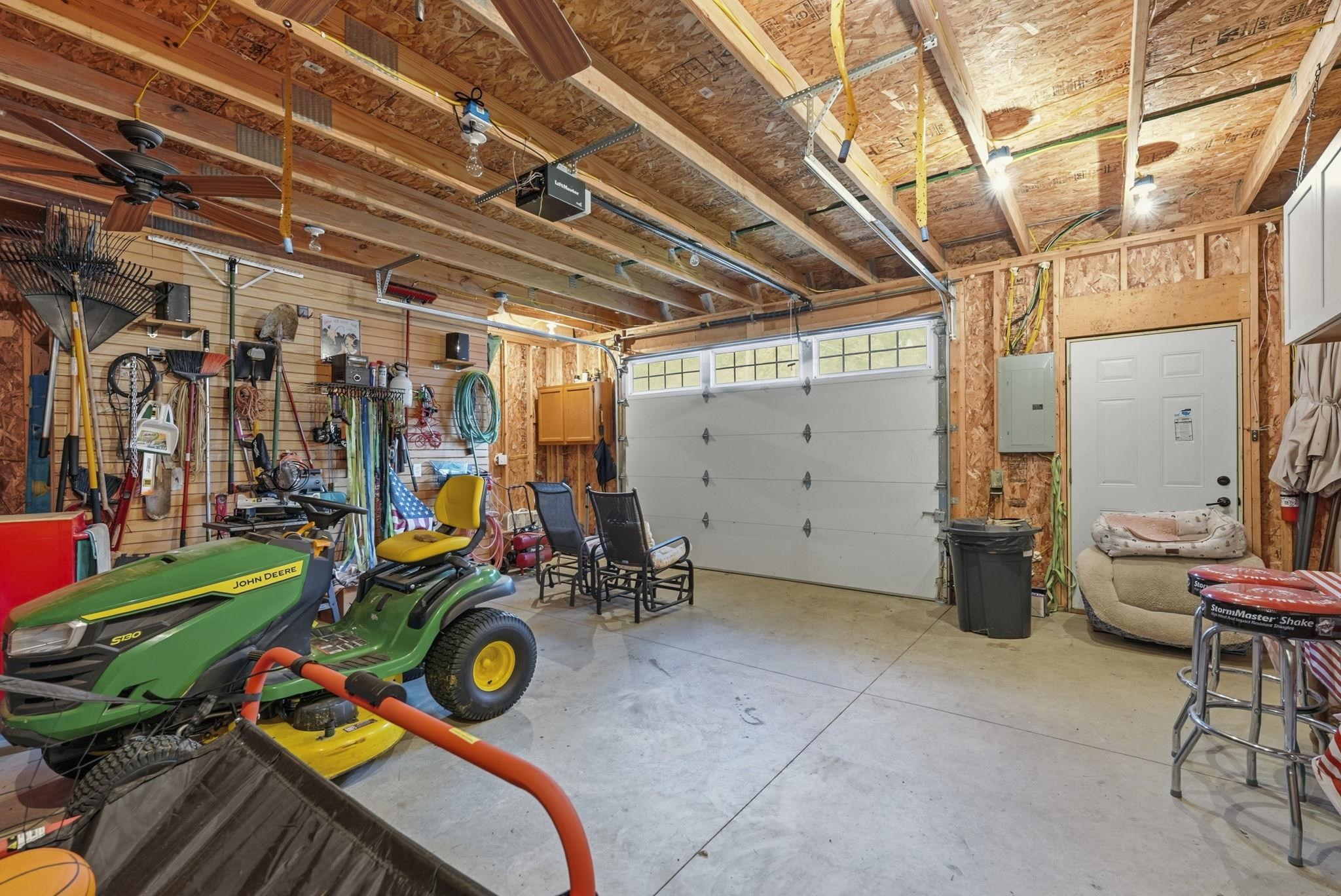 Attached garage featuring exposed wood framing, concrete flooring, and a white overhead door with transom-style windows