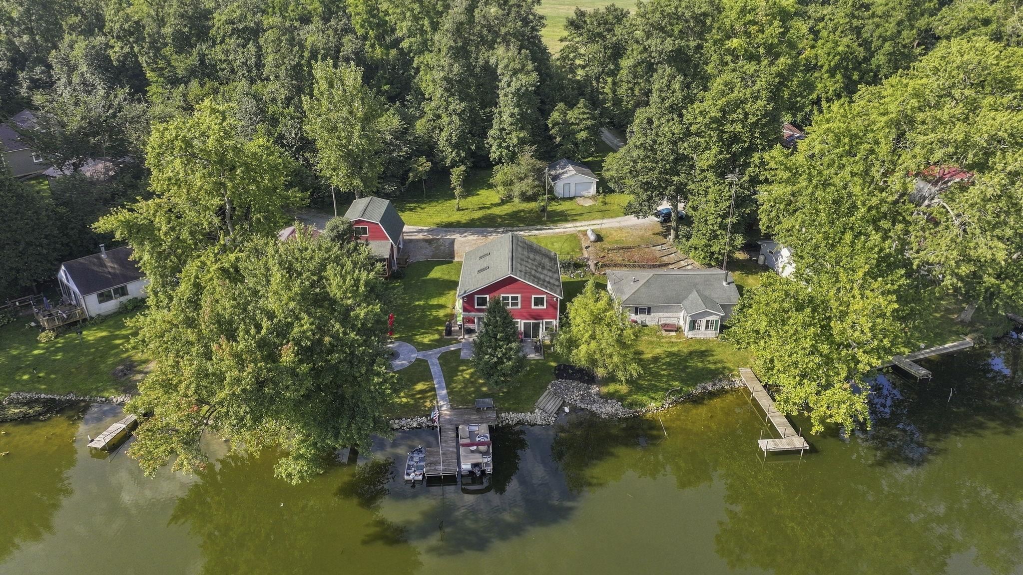 Waterfront property featuring a red house, an additional structure with a red roof, multiple docks, and mature trees