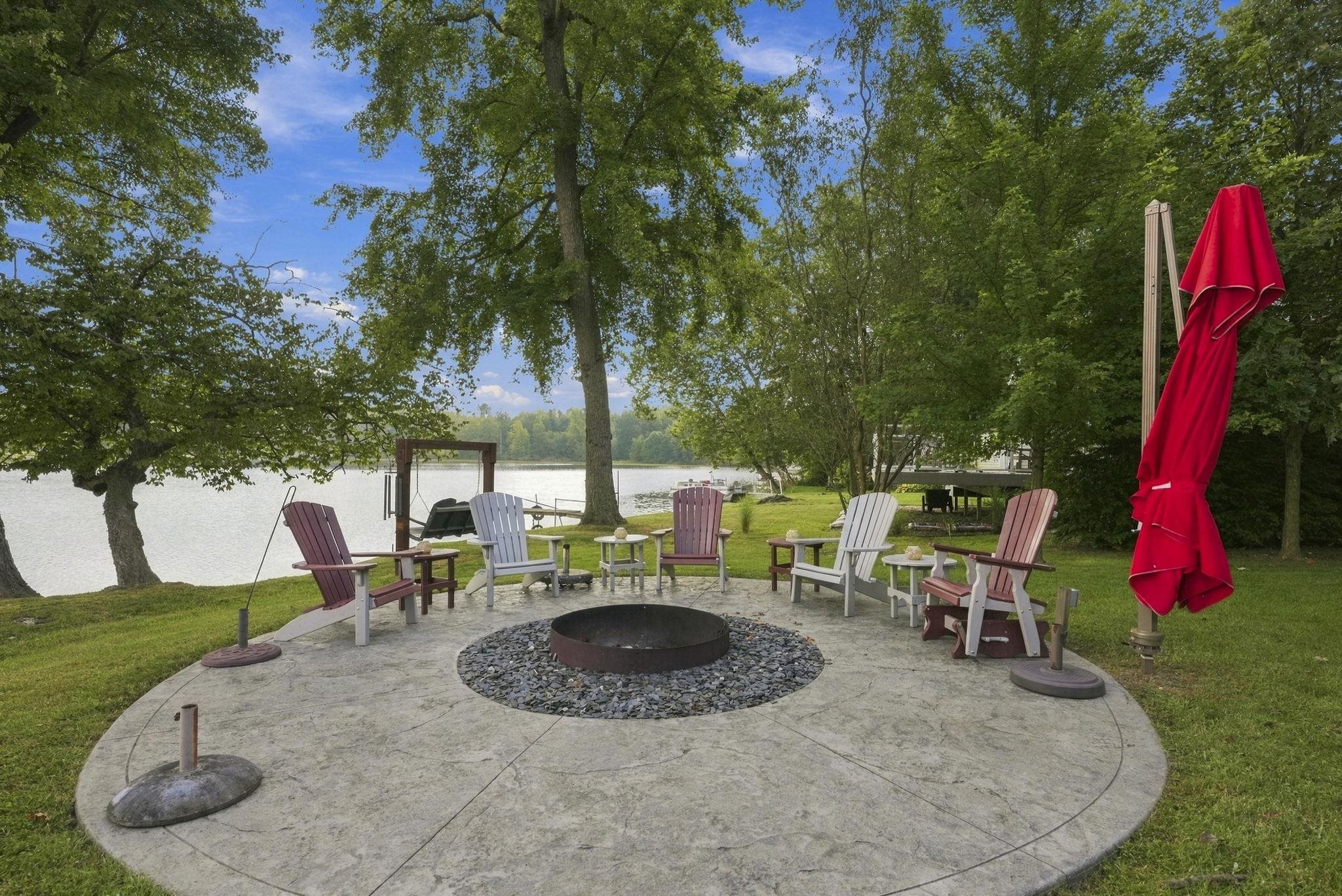 Stamped concrete patio with a central fire pit surrounded by a gravel inlay, expansive grassy area, and mature trees