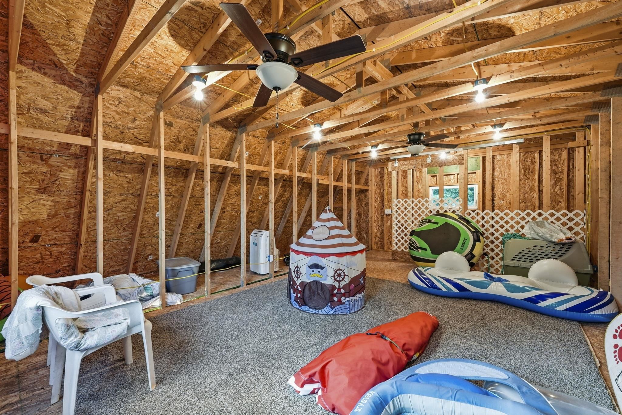 Unfinished space with visible wood framing, exposed plywood walls, two ceiling fans, and recessed lighting fixtures