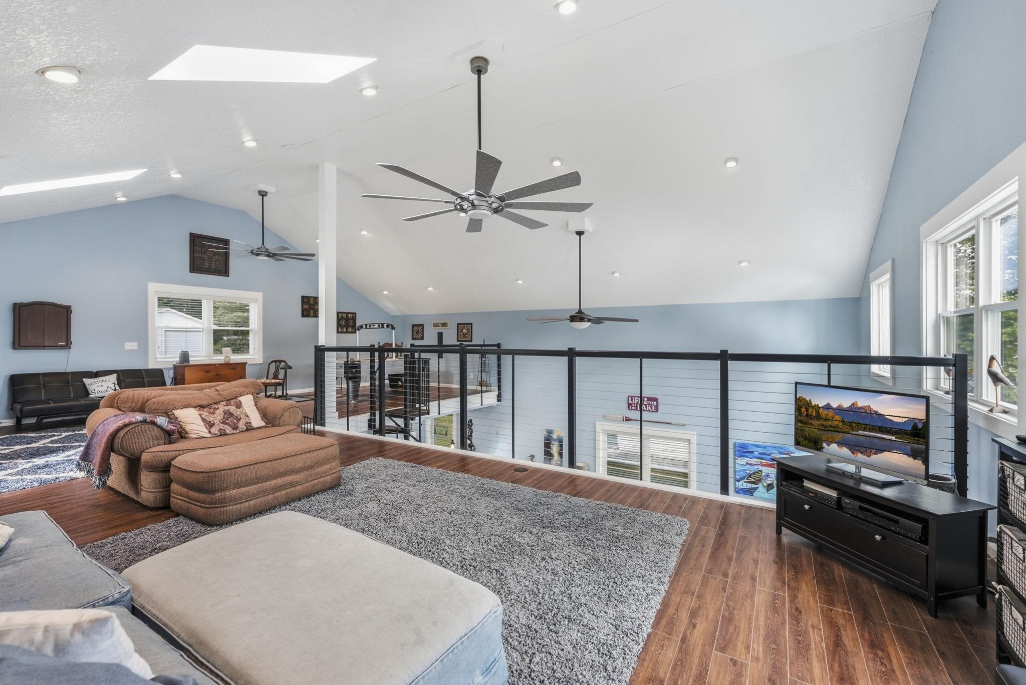 Vaulted ceiling with skylights, recessed lighting, wood-finish flooring, ceiling fans, and a glass-paneled railing