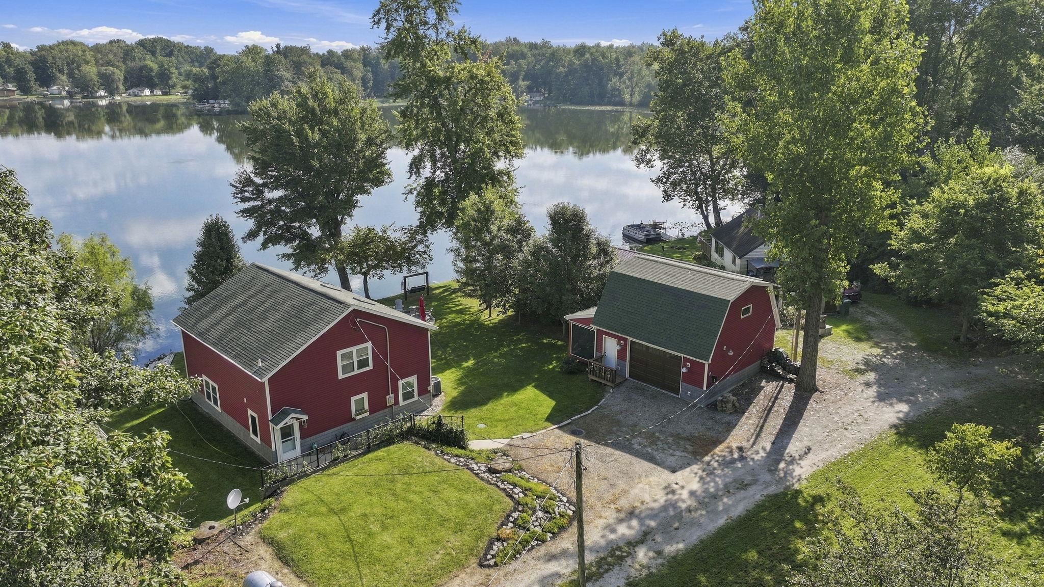 Waterfront property with a red exterior, green shingle roofing, and established trees