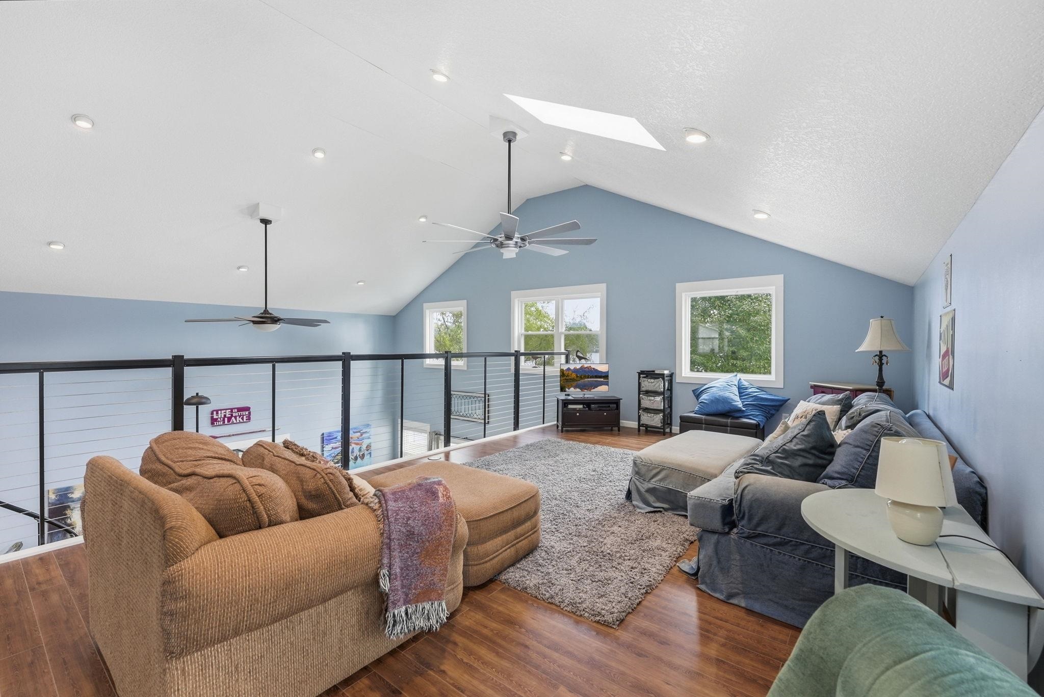 Vaulted ceiling with recessed lighting, wood-finish flooring, glass panel railing, and multiple windows