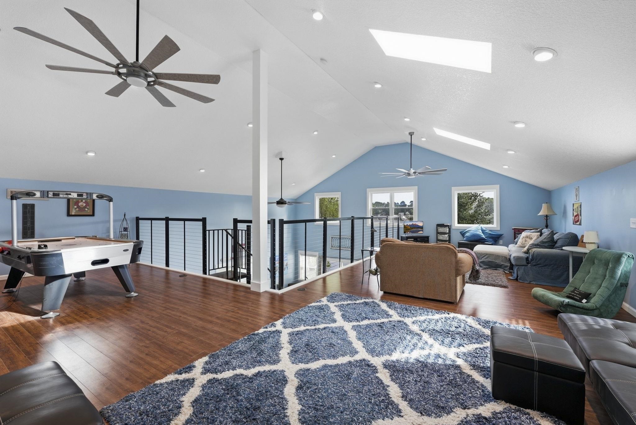 Vaulted ceilings with skylights, recessed lighting, wood-finish flooring, and open railing