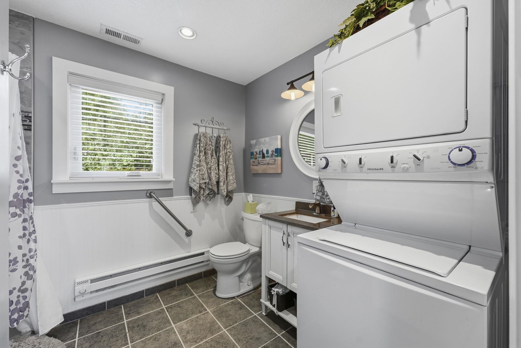 Full-size stacked washer and dryer, tile flooring, built-in vanity with countertop, and white wall paneling