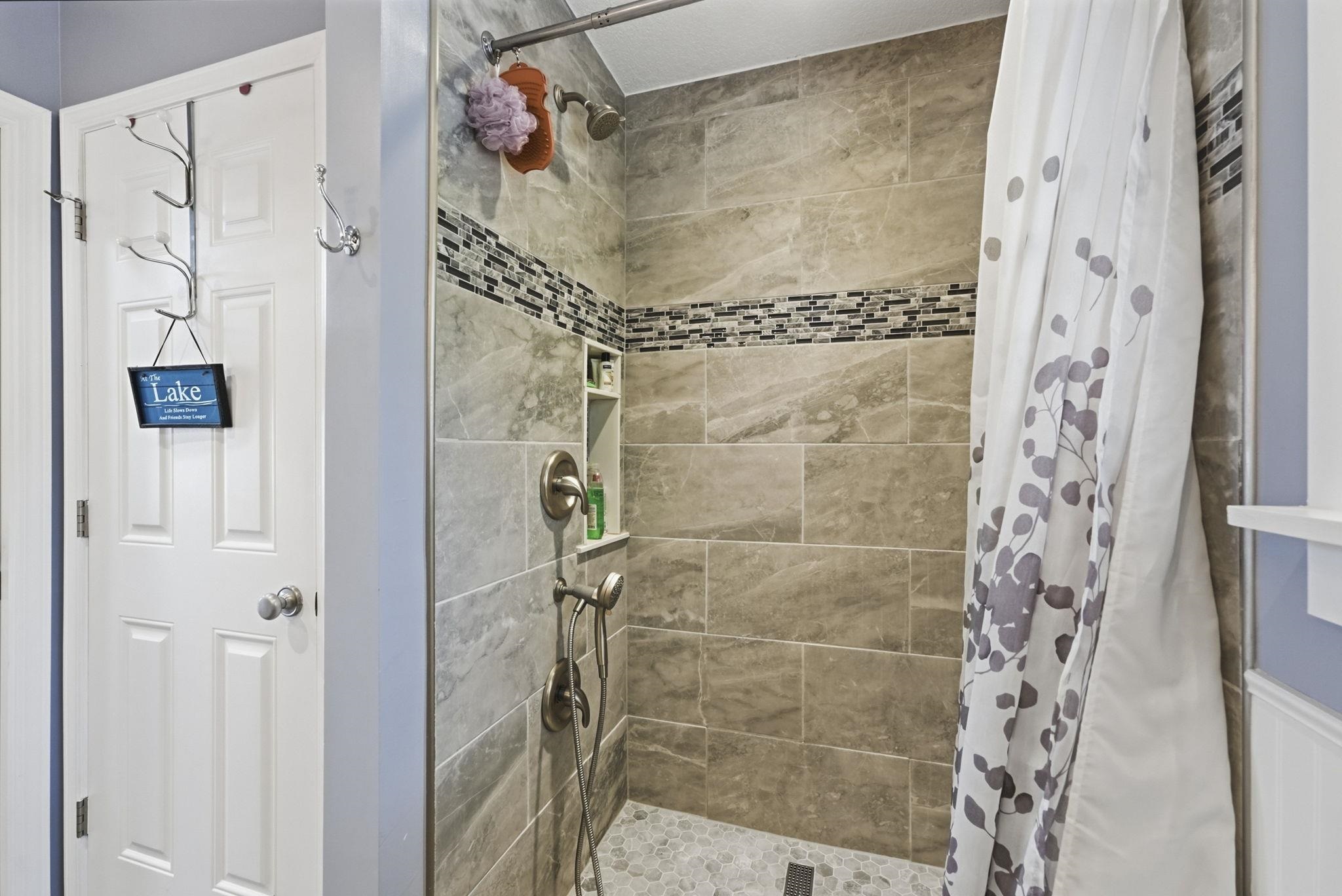 Tiled shower with a mosaic accent band, integrated recessed shelving, and a dual-function shower head