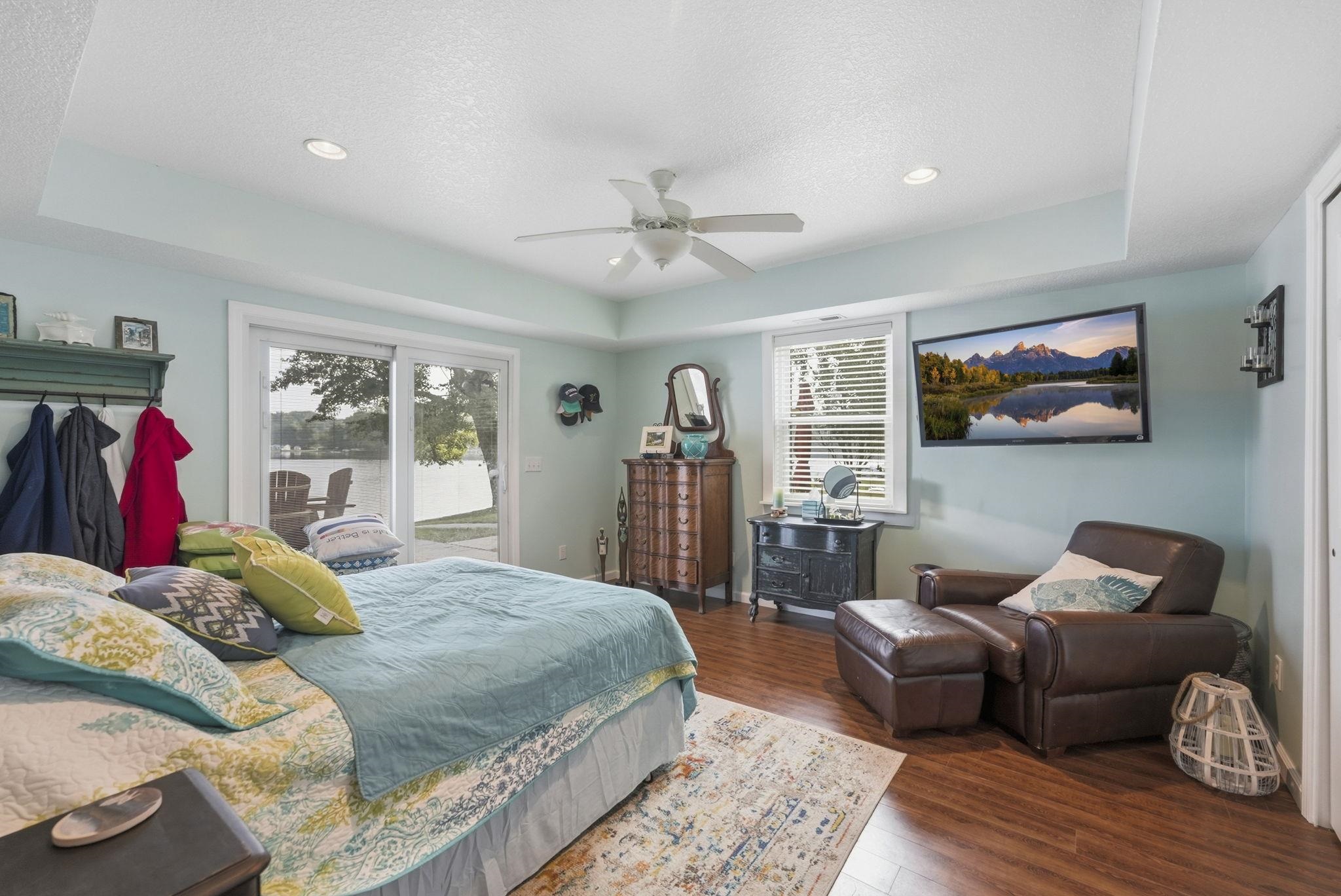 Tray ceiling with recessed lighting and ceiling fan, wood-finish flooring, sliding glass door, white window blinds, and light blue wall color