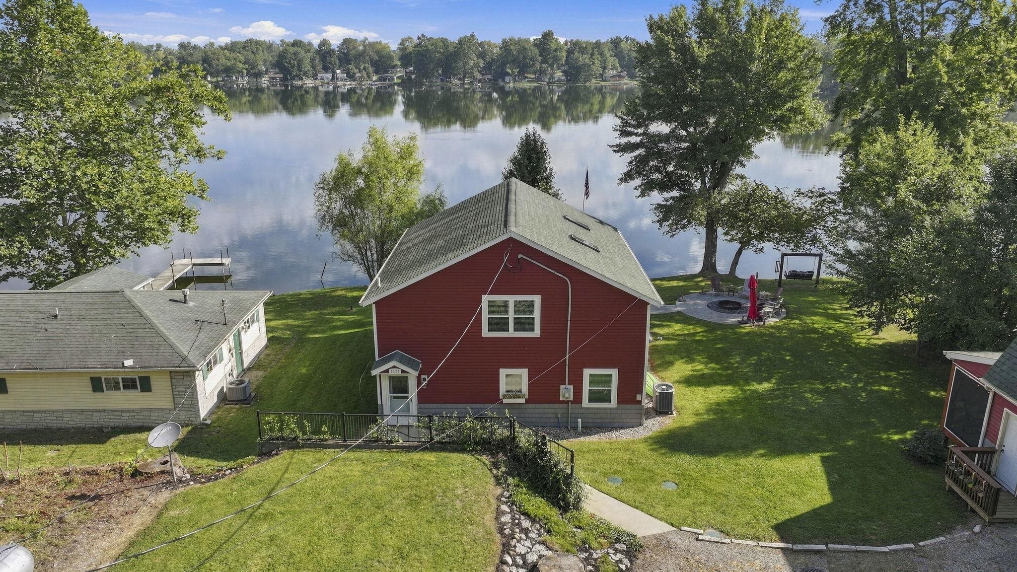Waterfront property featuring a red-sided structure with white window frames and a green roof