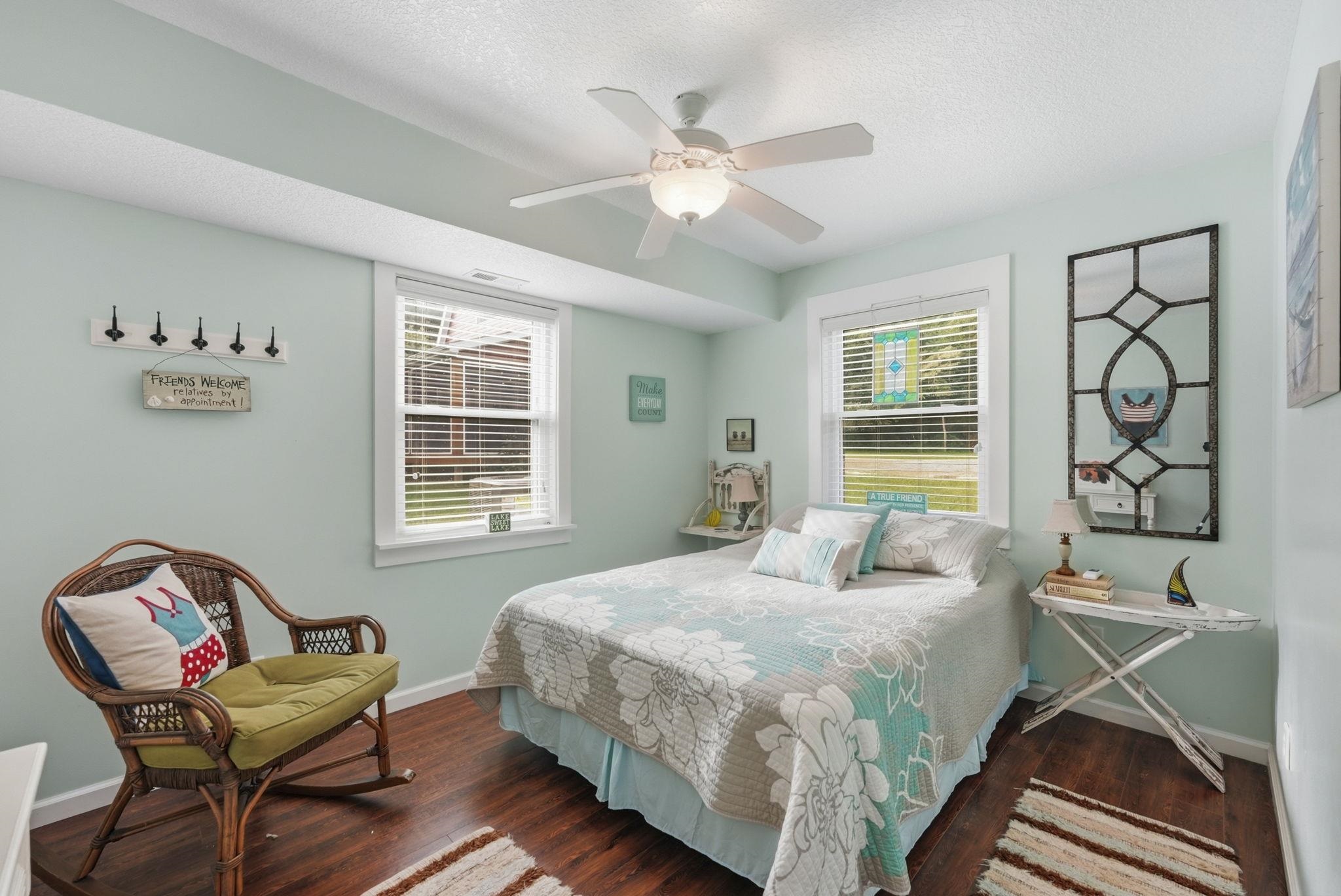 Wood-finish flooring, two windows with blinds, a ceiling fan with integrated lighting, and light-toned wall finishes