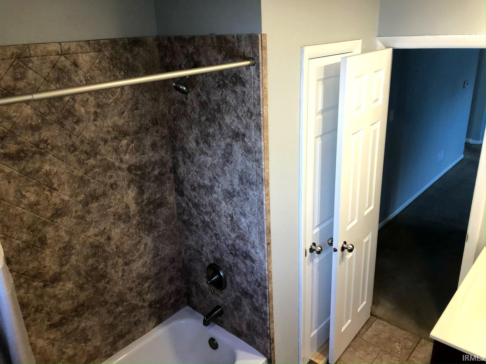 Tub/shower combination featuring dark textured wall surround and matte black fixtures