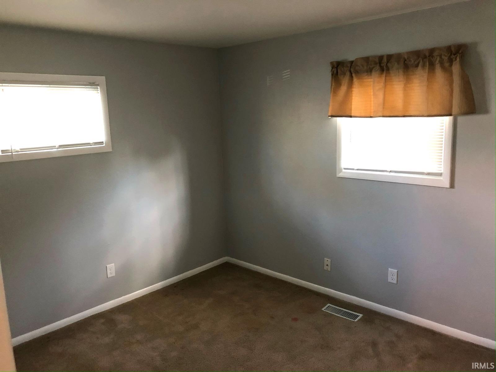 Neutral tone wall finish, two windows with white blinds, and carpeted flooring