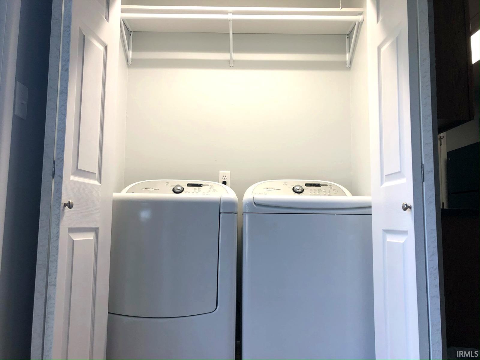 Laundry closet featuring bi-fold doors, white shelving, and a wall outlet