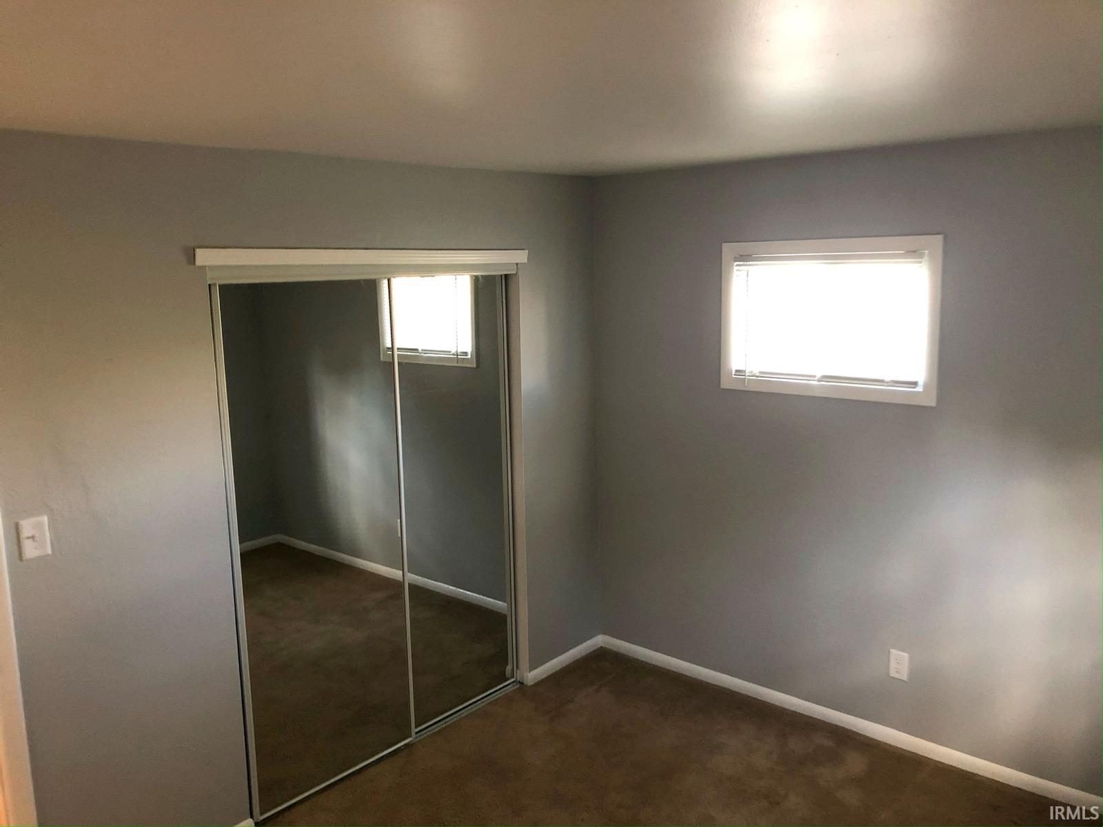 Mirrored closet doors, single window with blinds, light gray wall paint, and brown carpeting