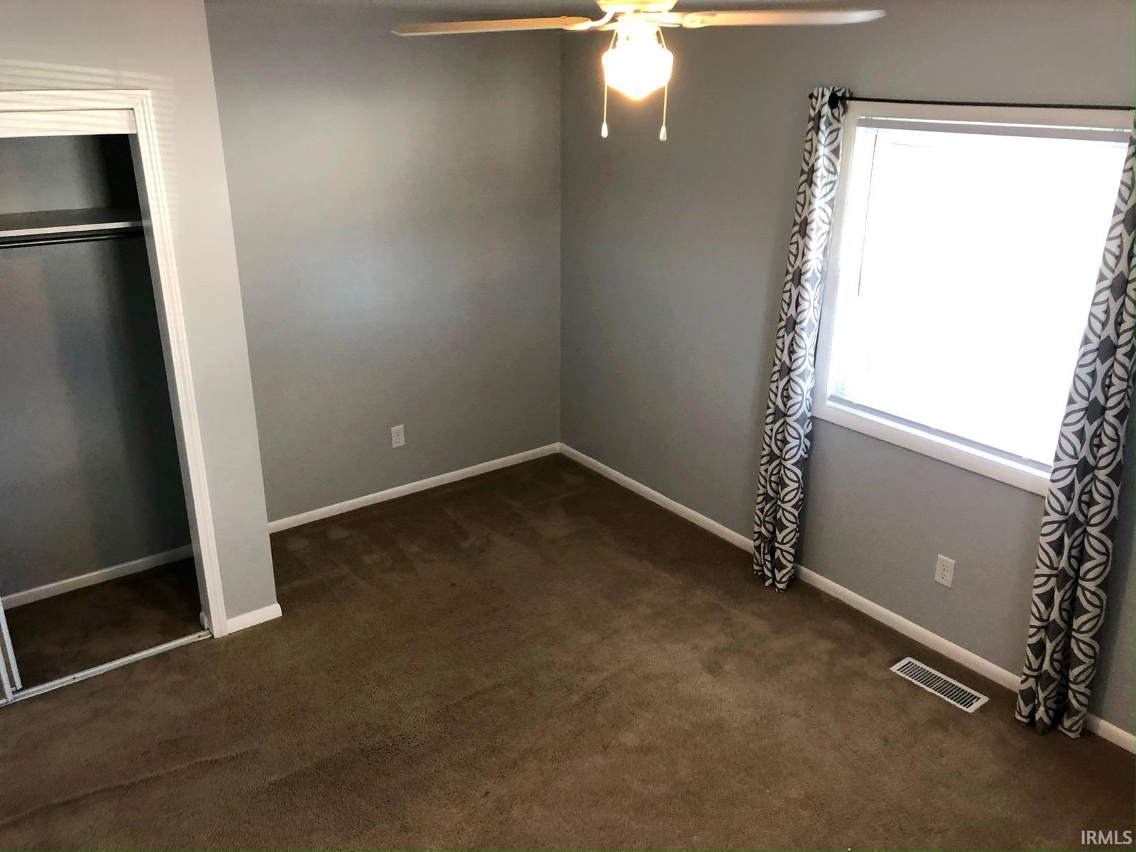 Carpeted flooring, neutral wall color, window, built-in closet with hanging rod, and ceiling fan with light fixture