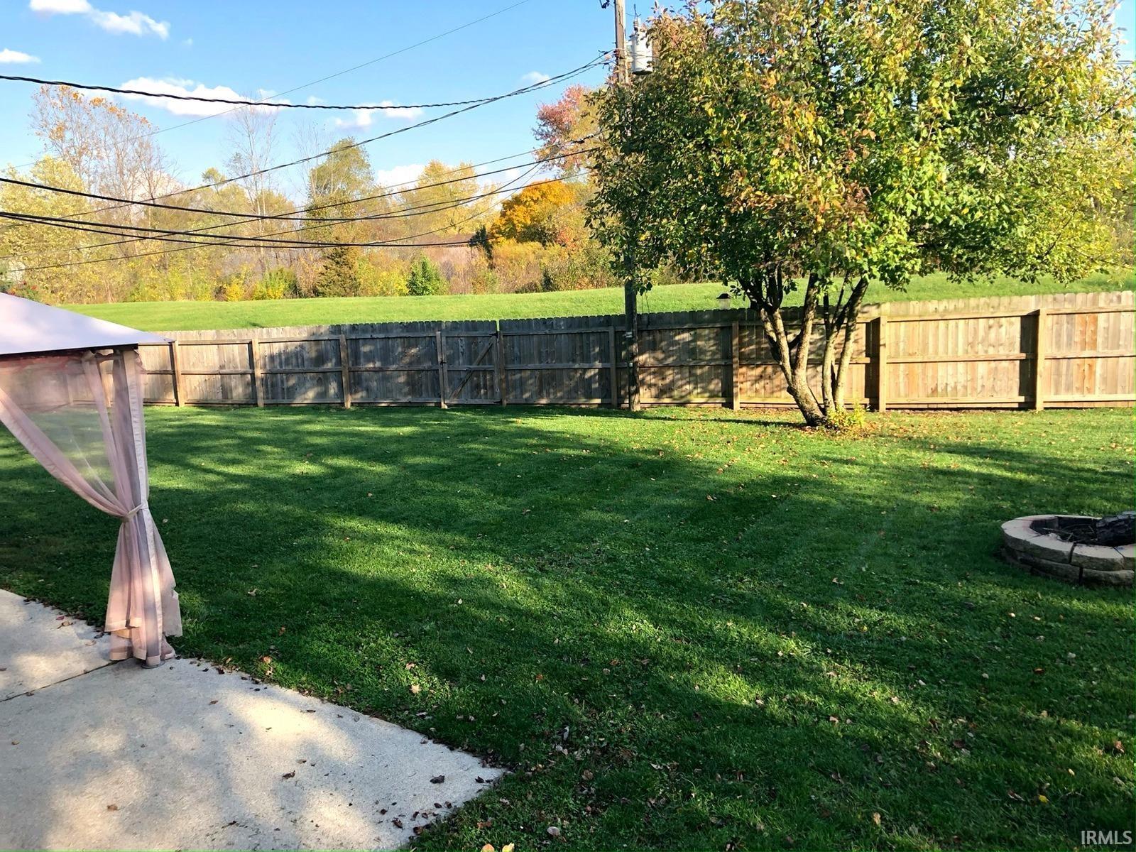 Expansive green lawn with a wood privacy fence, mature tree, and stone-ringed fire pit
