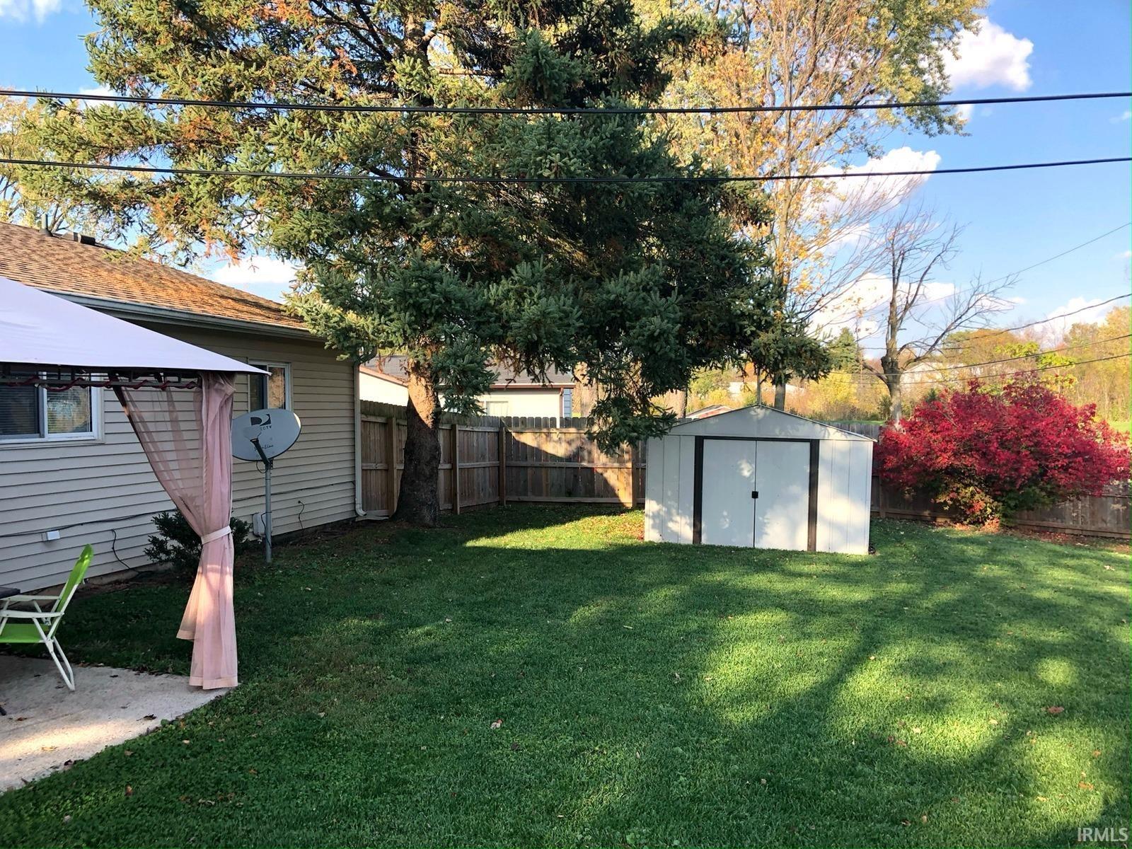 Expansive grassy yard featuring a wood privacy fence, mature trees, and a storage shed