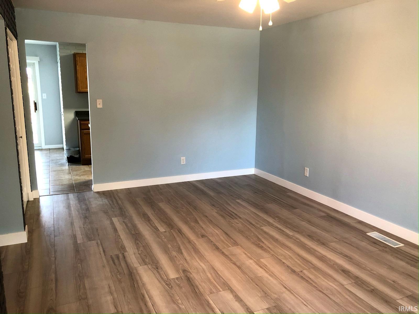 Wood-finish flooring, light blue wall paint, white trim, and a ceiling fan with integrated lighting