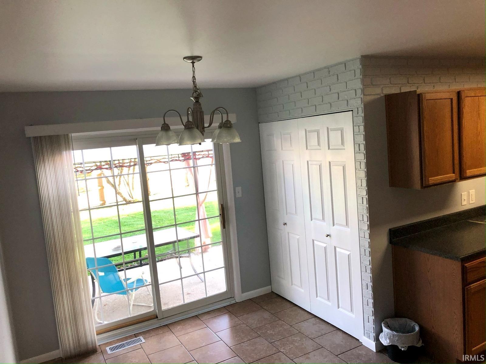 Sliding glass door leading to outdoor space, tile flooring, built-in bi-fold closet, wood-finish cabinetry, and a ceiling-mounted light fixture