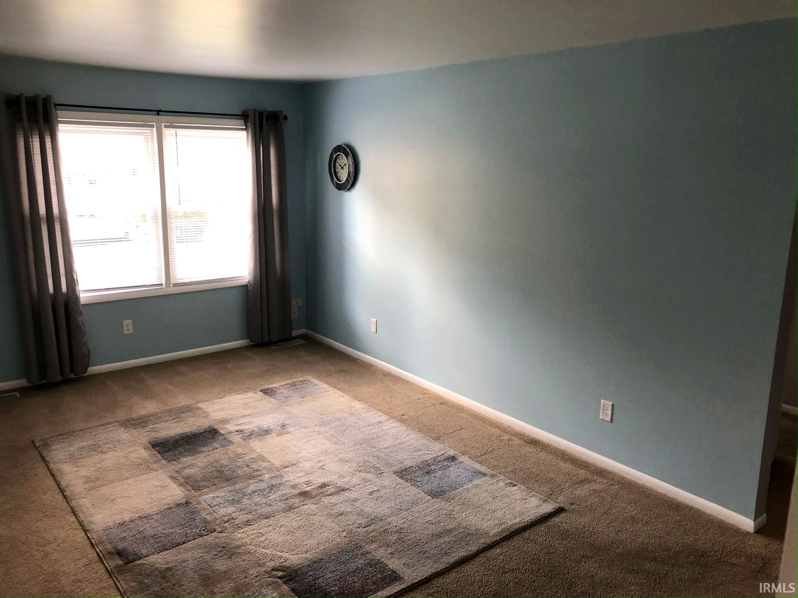 Carpeted flooring, light blue painted walls, and window with blinds