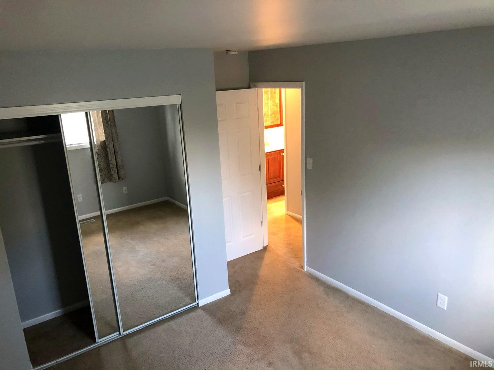 Carpeted flooring, light grey wall paint, and mirrored closet doors