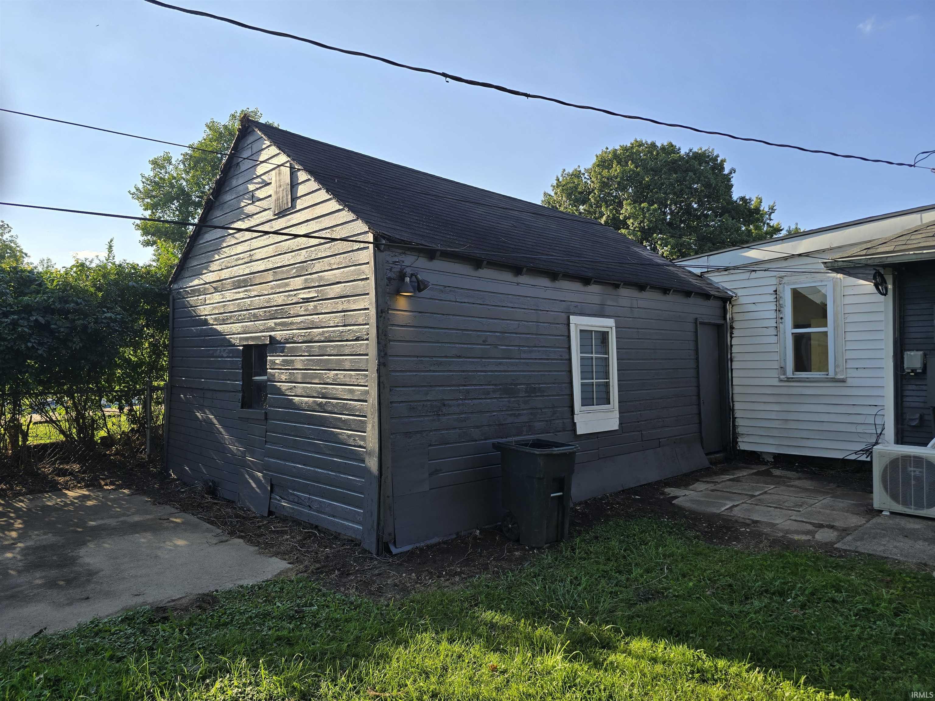 Detached outbuilding with horizontal siding, a gabled roof, and a single-pane window
