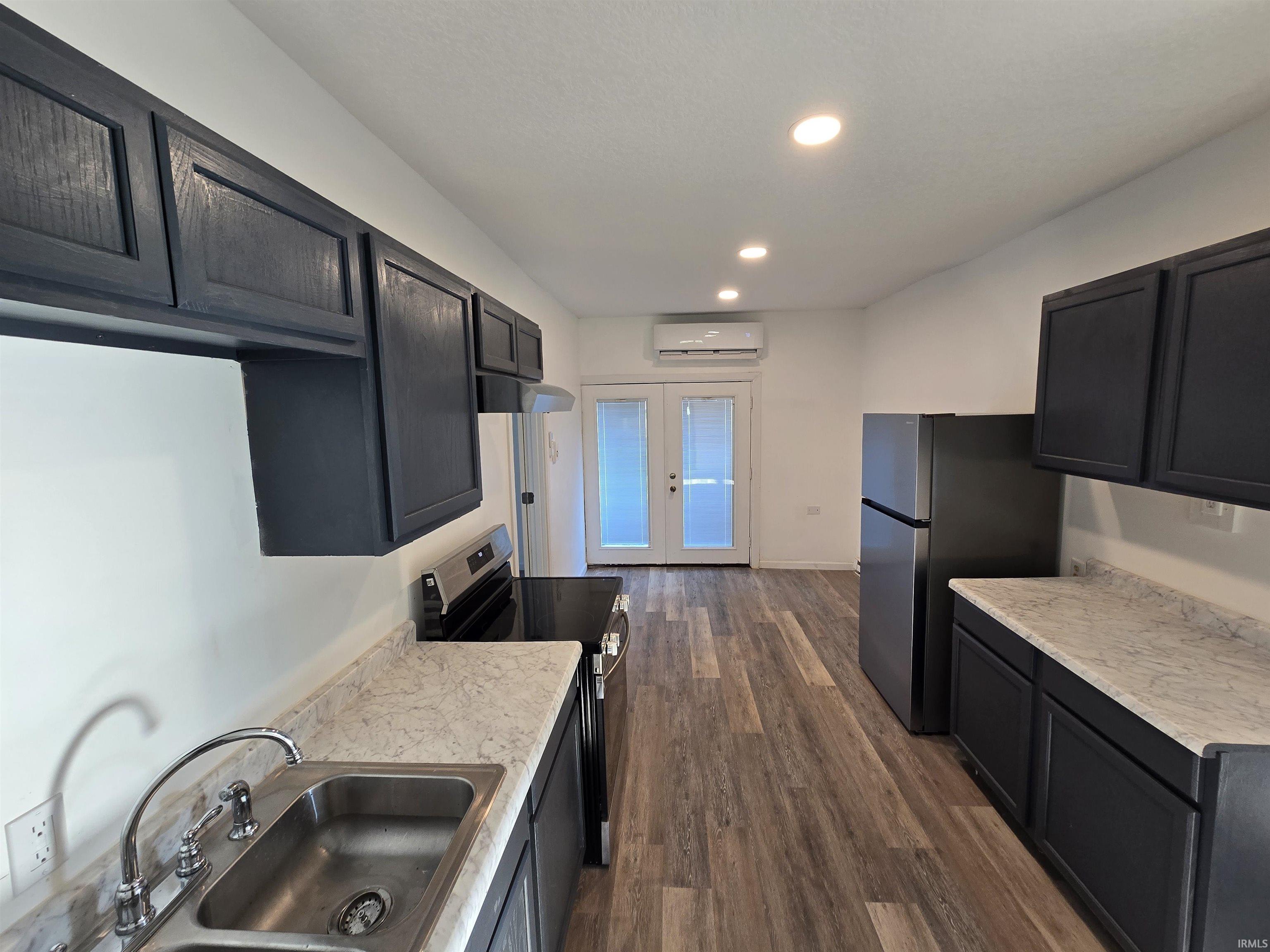 Kitchen featuring dark cabinetry, light-toned countertops, a stainless steel sink, and wood-finish flooring