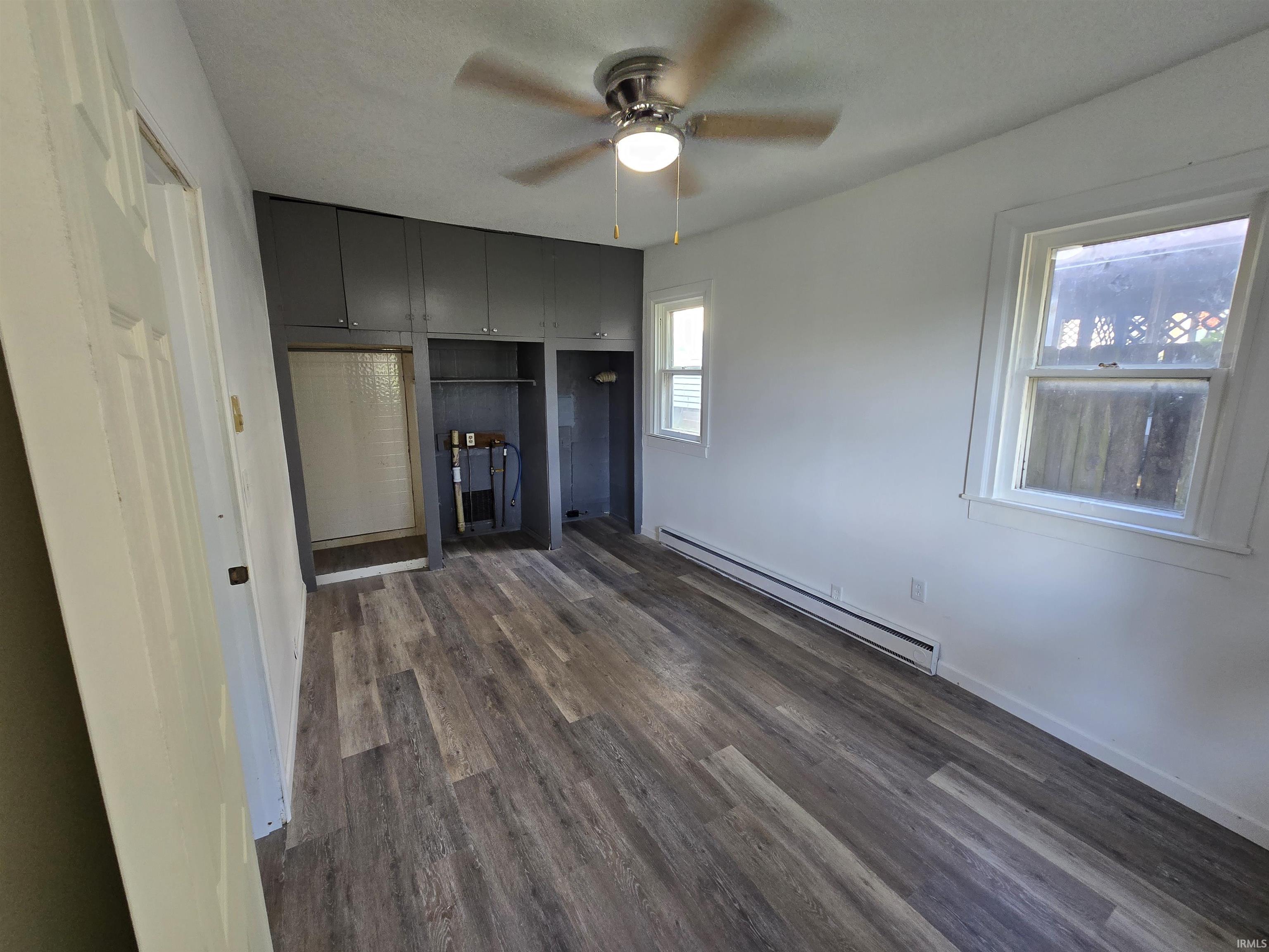 Wood-finish flooring, two windows, ceiling fan with integrated lighting, and built-in cabinetry with open shelving