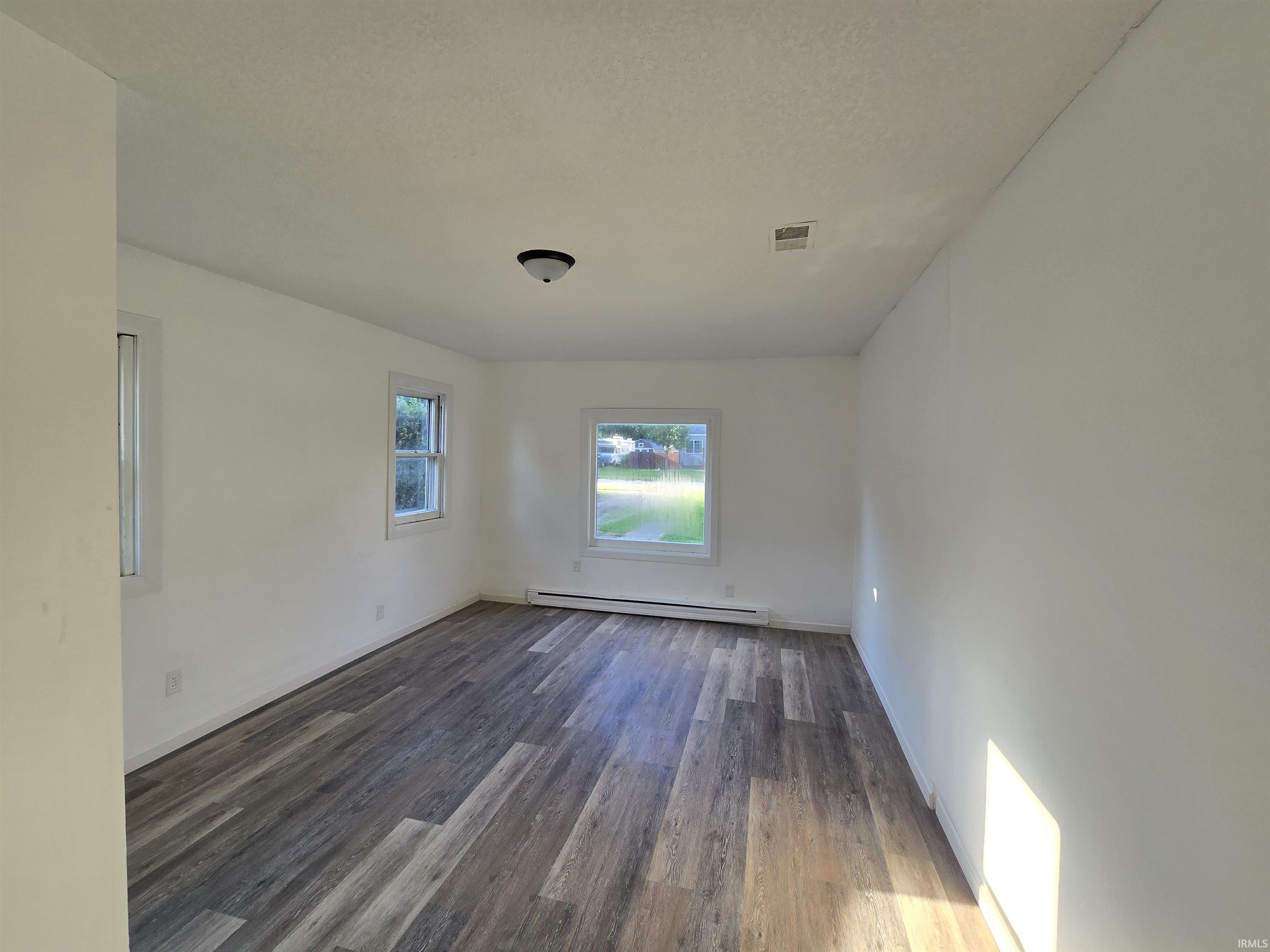 Spacious room featuring wood-finish flooring, white walls, and multiple windows