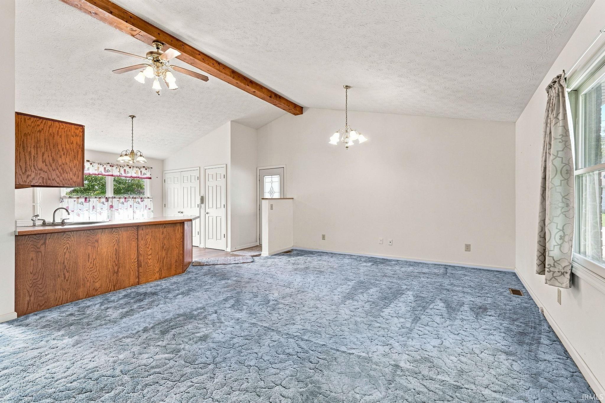 Vaulted ceiling with exposed wood beams, overhead ceiling fan, and wall-mounted lighting fixtures