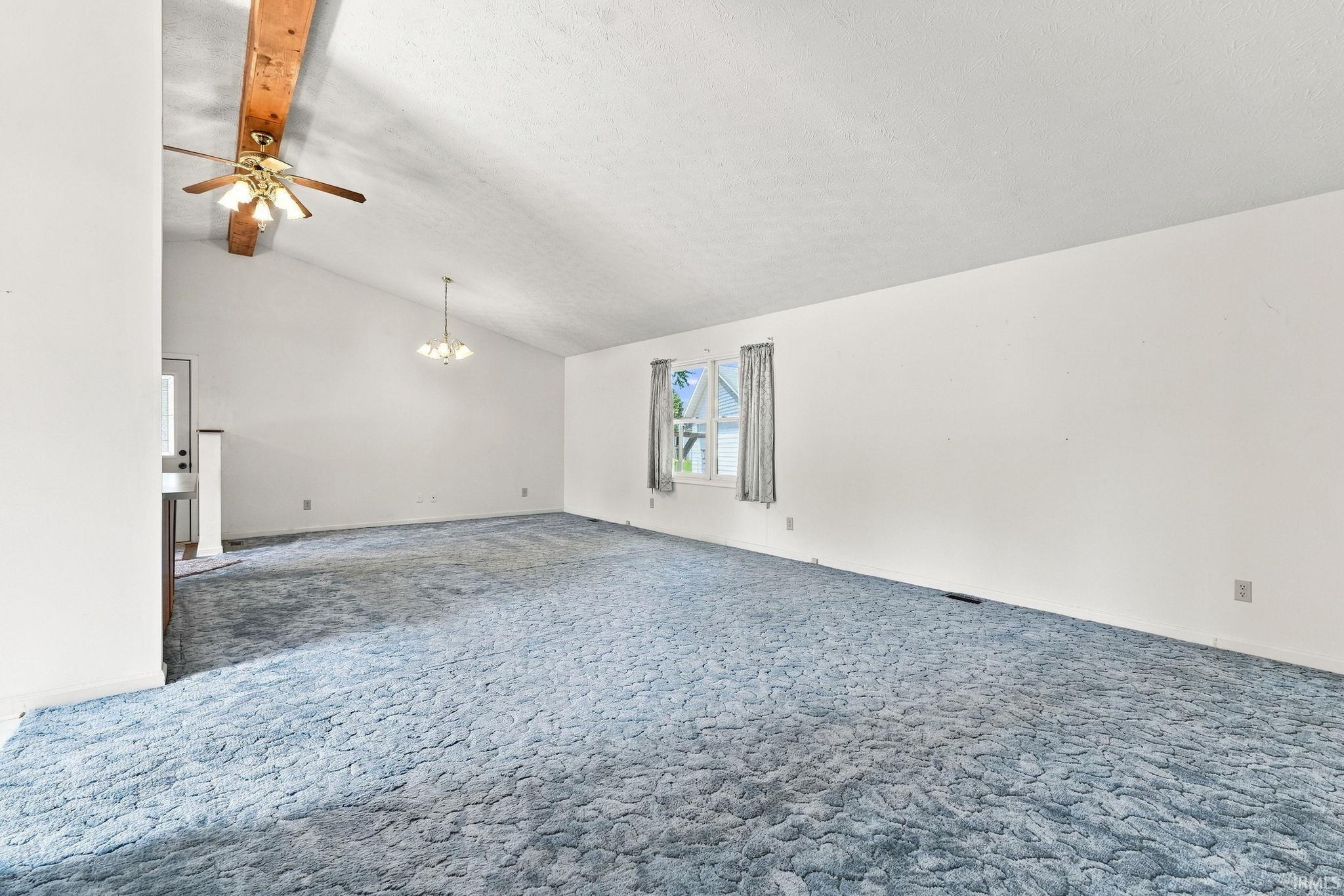 Vaulted ceiling with exposed wood beam, ceiling fan, and chandelier