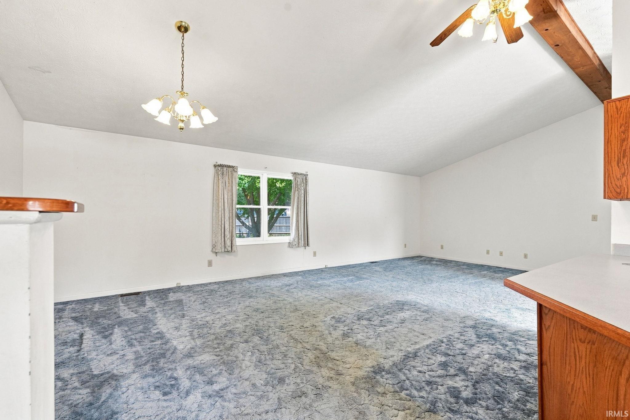 Vaulted ceiling with an exposed wood beam, window with exterior landscape, carpeted flooring, and a kitchen pass-through counter with wood-finish cabinetry