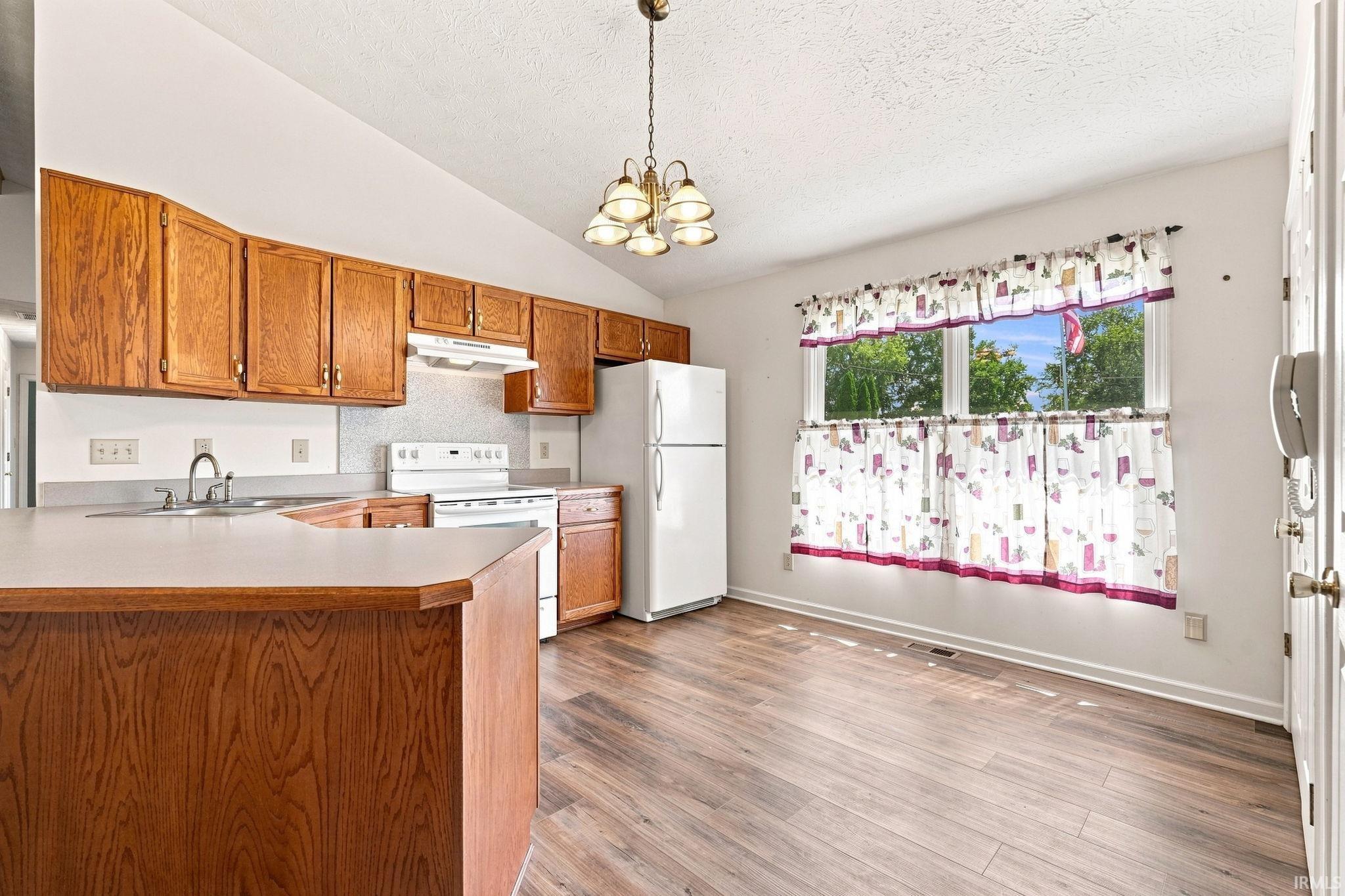 Kitchen featuring wood-finish cabinetry, white appliances, and a vaulted ceiling